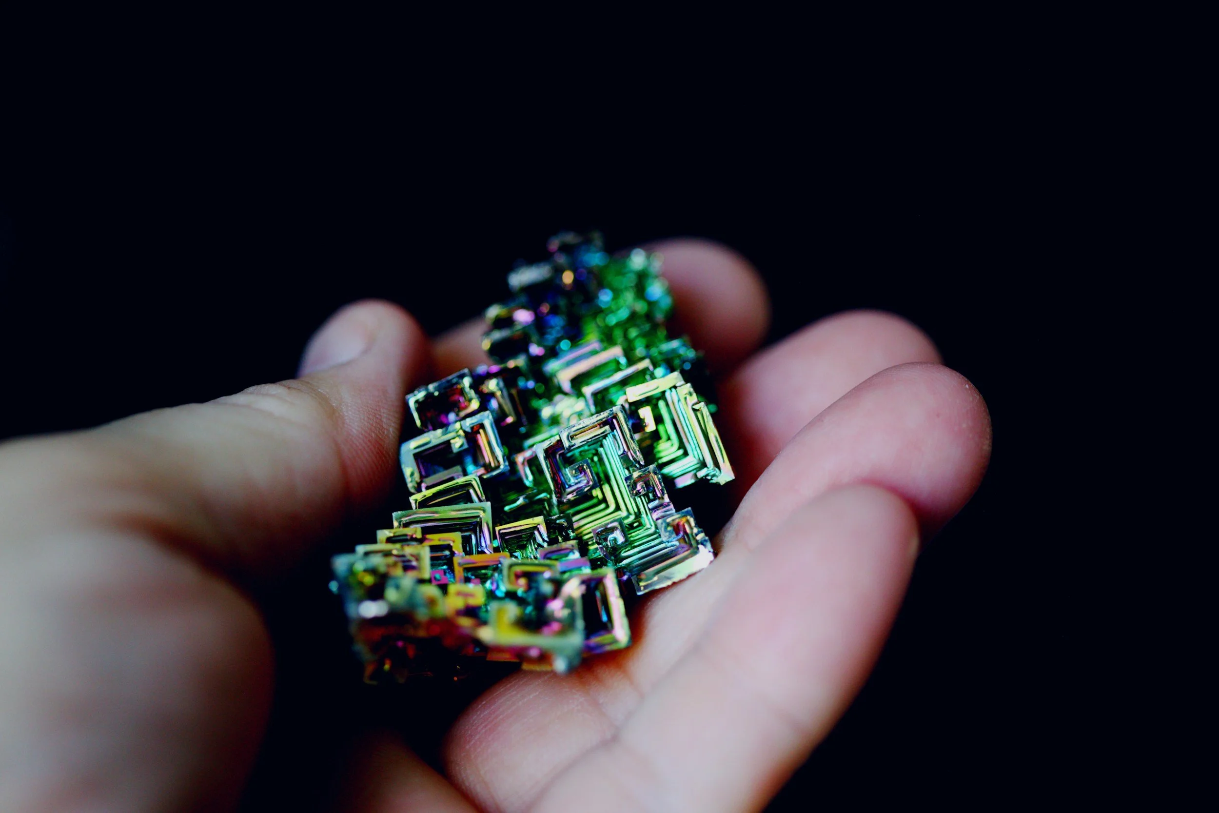 An iridescent Bismuth crystal with geometric, stair-step formations and rainbow-coloured surfaces.