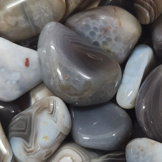 A polished Botswana Agate stone with soft grey, brown, and cream banding in layered patterns.
