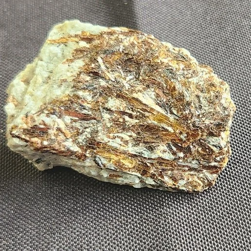 Astrophyllite stone with golden-bronze starburst patterns radiating through a dark matrix, showing a striking, reflective mineral texture.