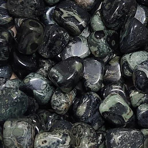 Dark green and black Kambaba Jasper stone with distinctive circular orb patterns, shown polished and tumbled.