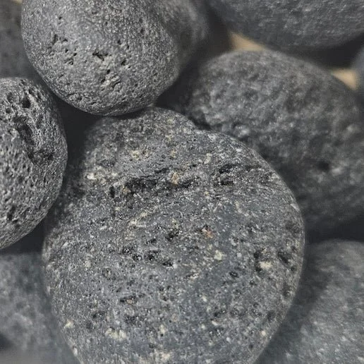 Black porous lava stone with natural volcanic texture, shown as both raw rock and polished beads.