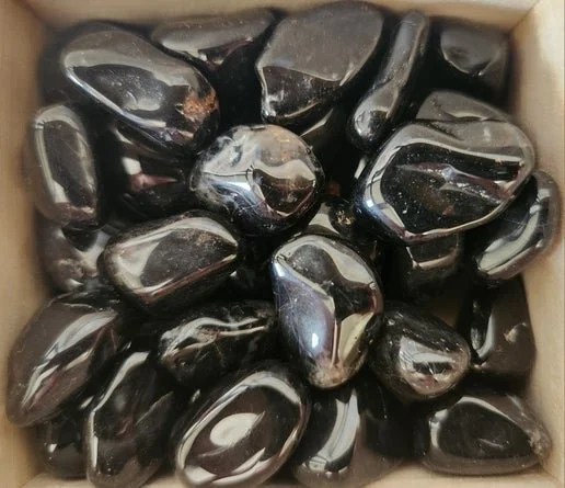 Polished and raw black Onyx stones including a smooth sphere and tumbled pieces with deep glossy black surface.