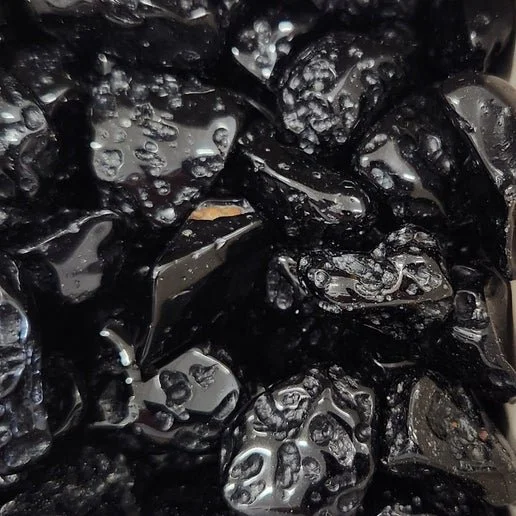 Natural black Tektite stones in raw and polished forms showing textured surface and impact glass appearance.