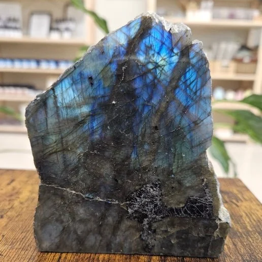 Polished labradorite stone displaying vibrant blue and green labradorescent flash against a natural crystal surface.