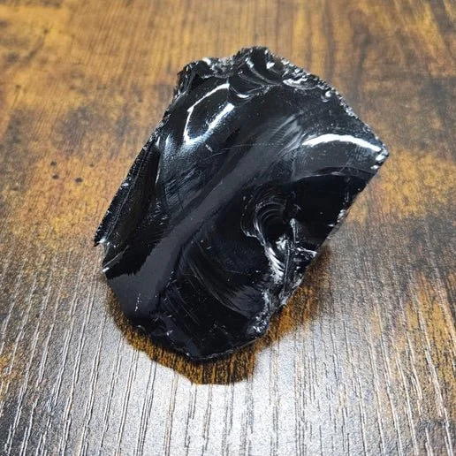 Polished and raw black Obsidian stones including a sphere and arrowhead, showcasing glossy volcanic glass texture.