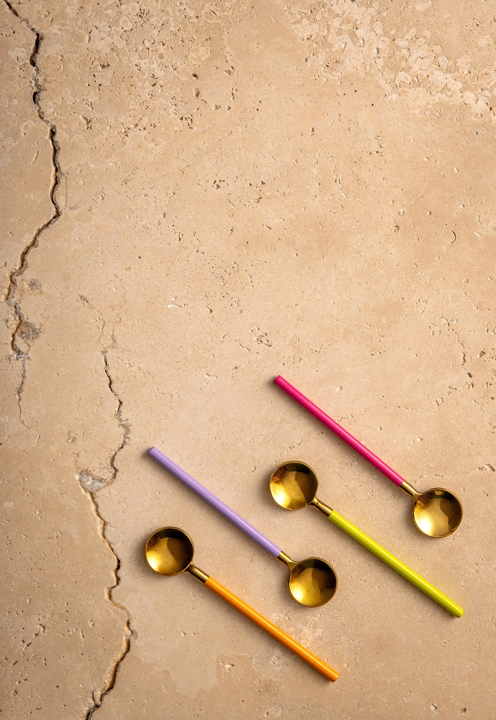Colorful measuring spoons and stirring sticks on a beige cracked concrete surface.