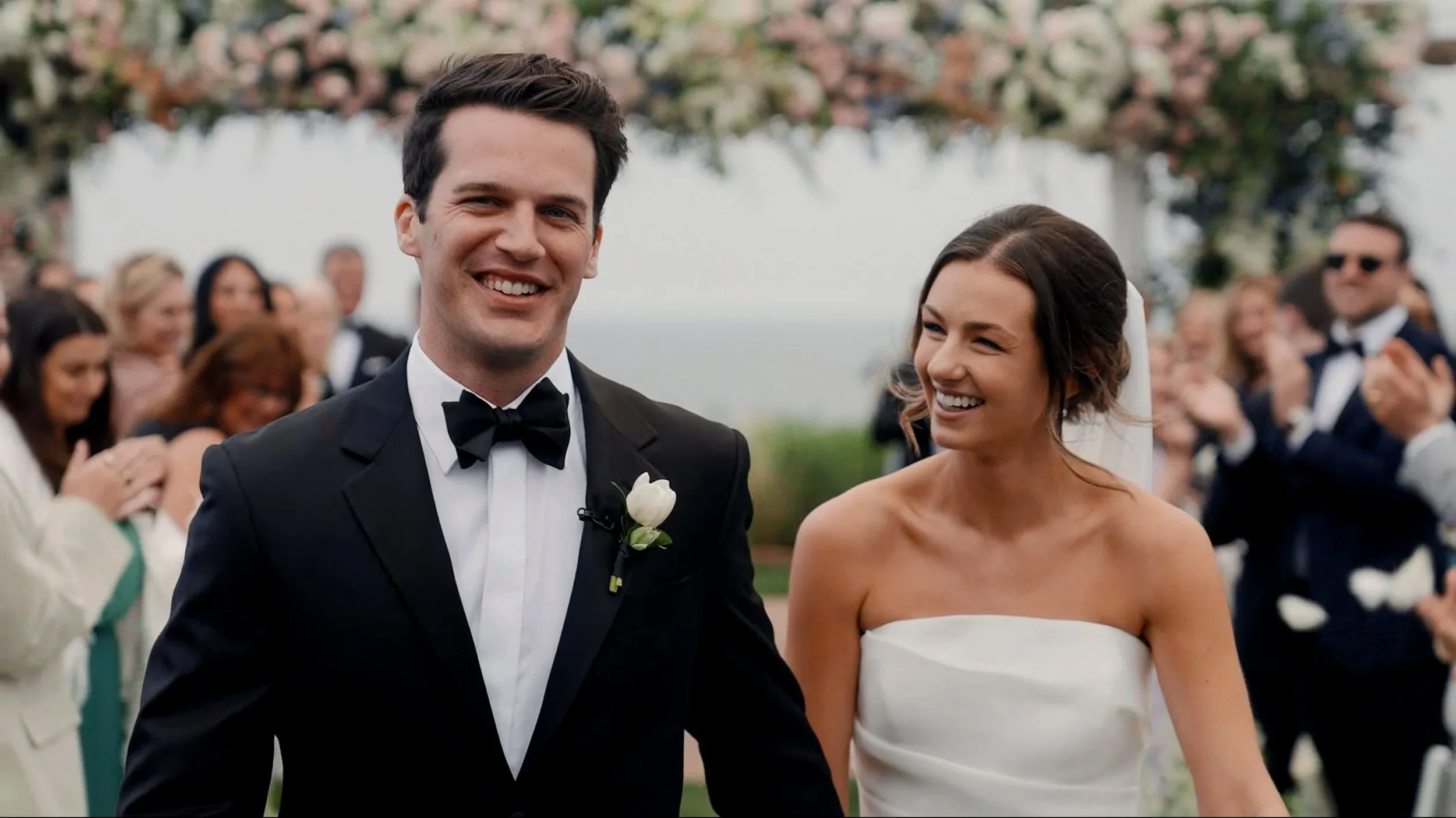 A happy couple getting married at an outdoor wedding ceremony, surrounded by guests.