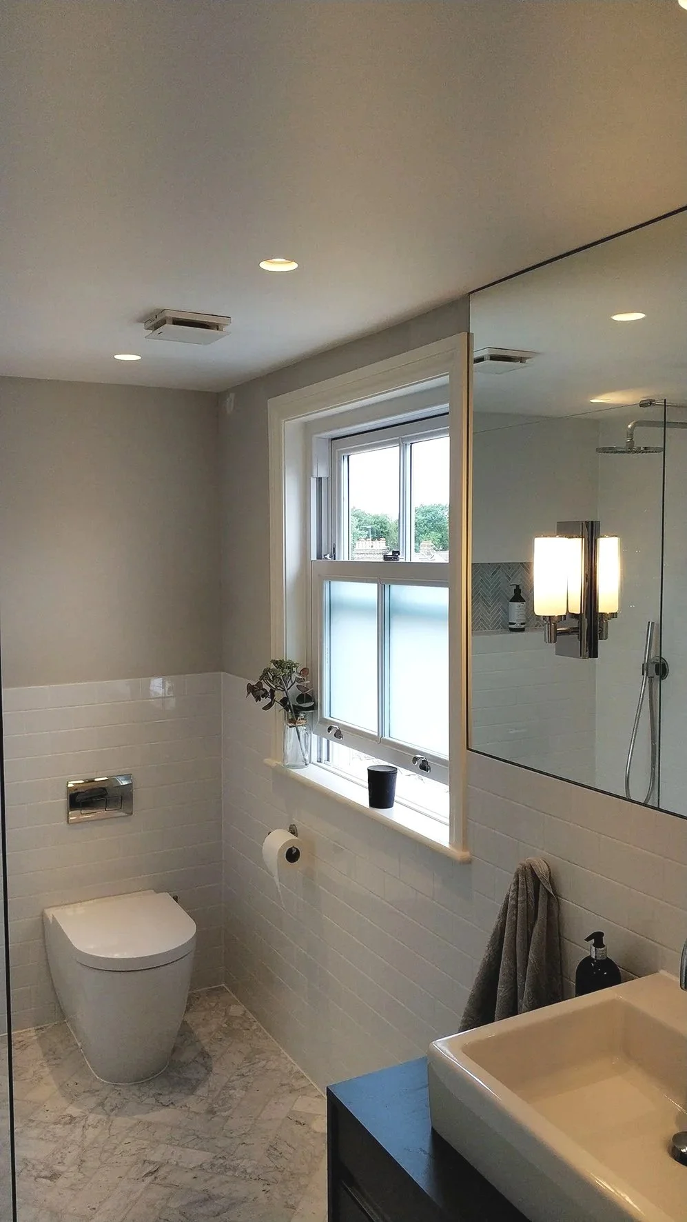 Modern bathroom with electric underfloor heating, concealet cystern toilet, large wall mirror and wall mood lighting.