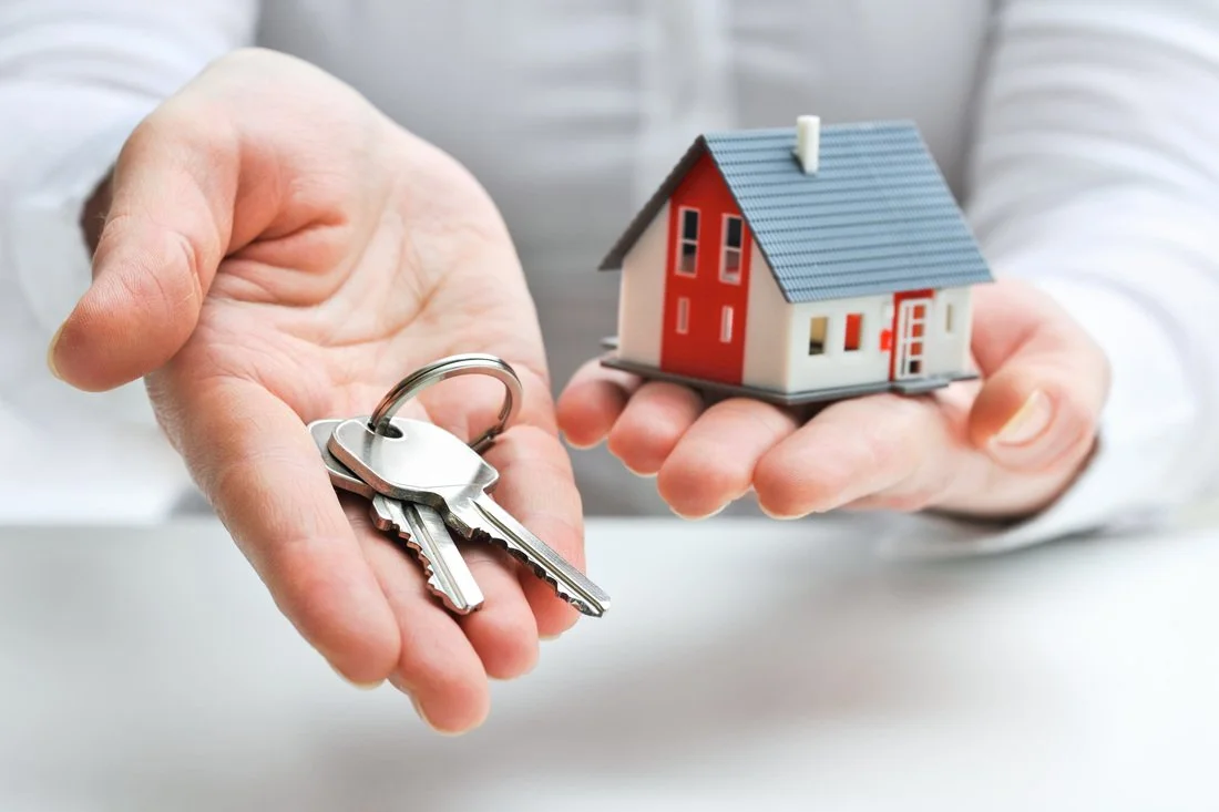 Person holding a set of house keys and a miniature model of a house.
