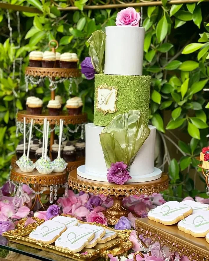 Styled dessert table with a green and white cake, cupcakes and cookies