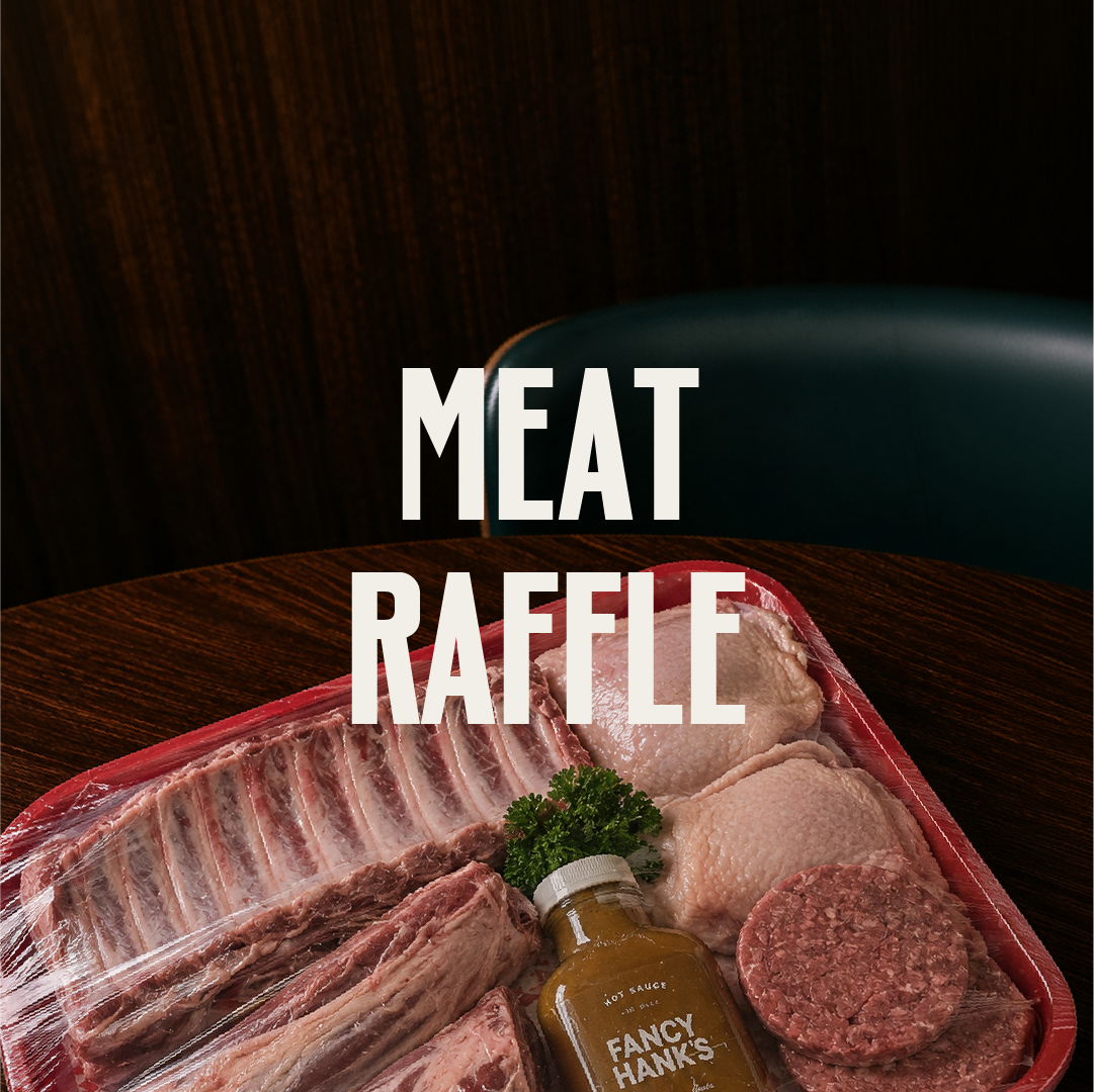A tray of raw meats including ribs, chicken, ground beef patty, and beef chunks, with a bottle of mustard labeled 'Fancy Hank's' and a small bunch of parsley, on a dark wooden table with a green chair in the background. Text overlay reads 'Meat Raffle.'
