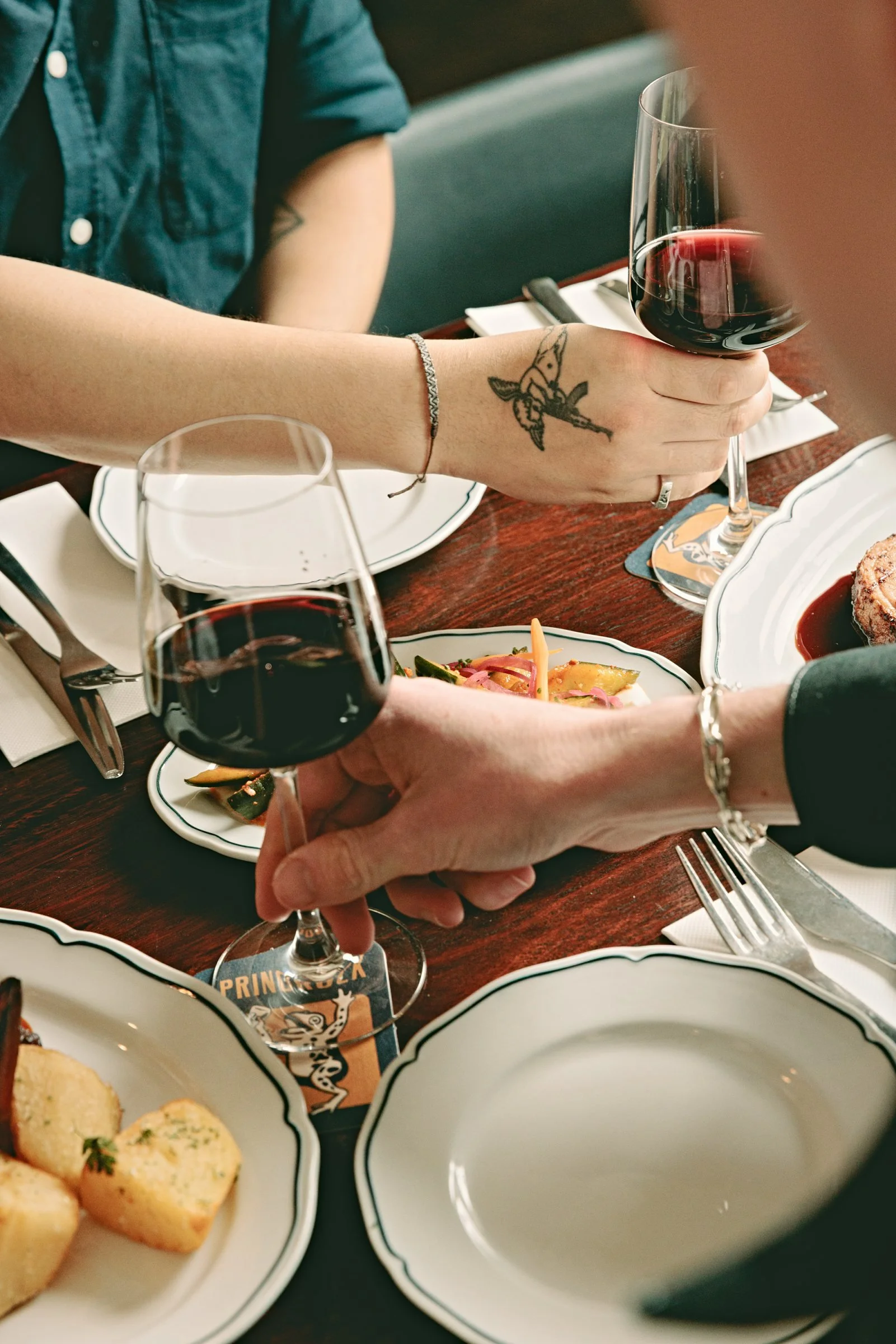 Two glasses of red wine passed across a table set with counter meals and Springrock coasters