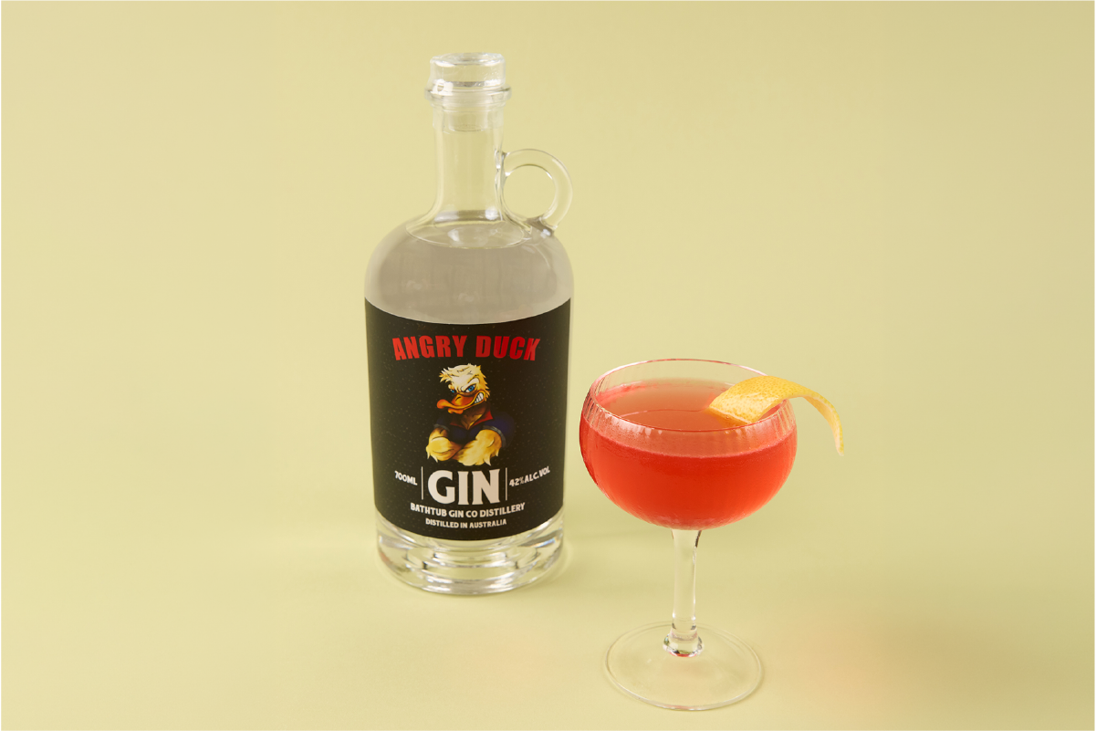 A bottle of Angry Duck gin and a cocktail with a lemon twist on a pale yellow background.