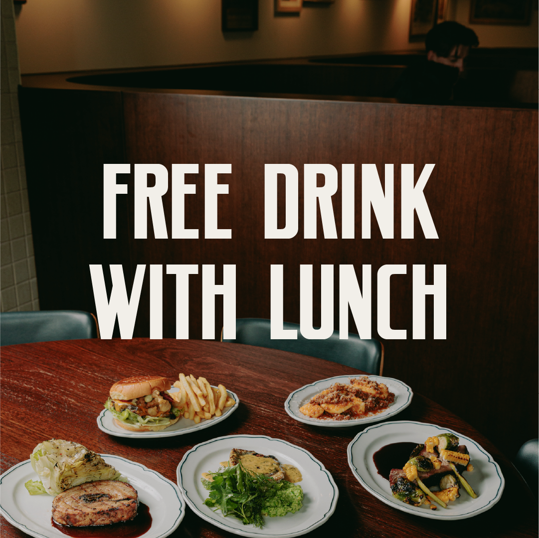 A wooden table with five plates of food, including a burger with fries, grilled meat with a sauce, a salad, and three other dishes, with a sign saying "Free Drink with Lunch" in large white letters.