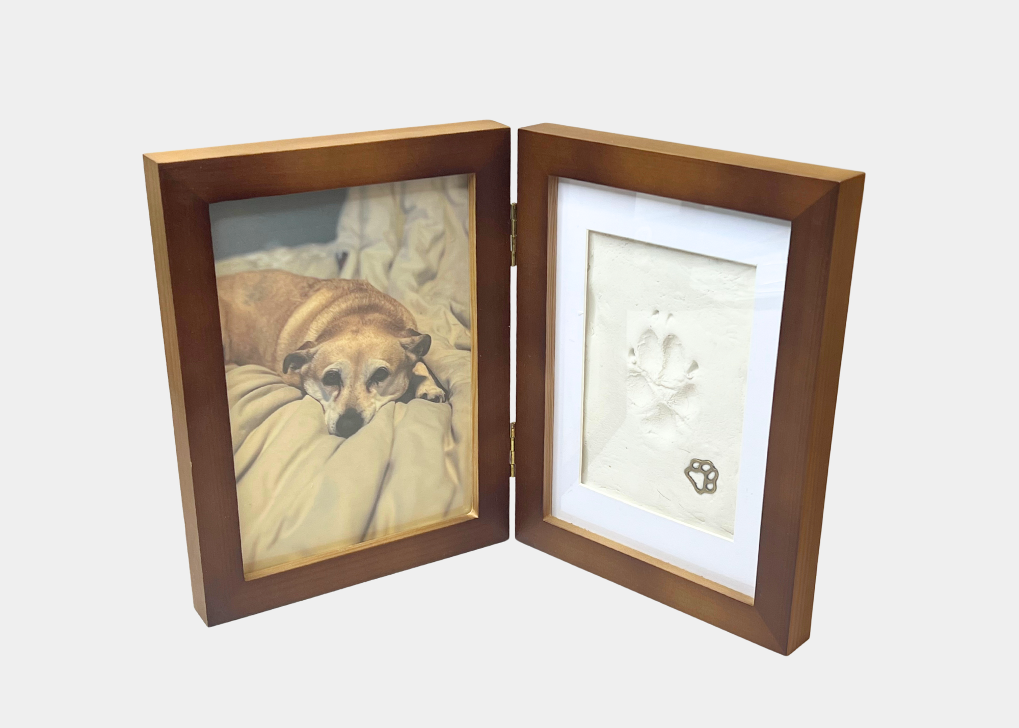 A wooden picture frame holding a photograph of a resting dog on the left and a paper with a paw print impression on the right.
