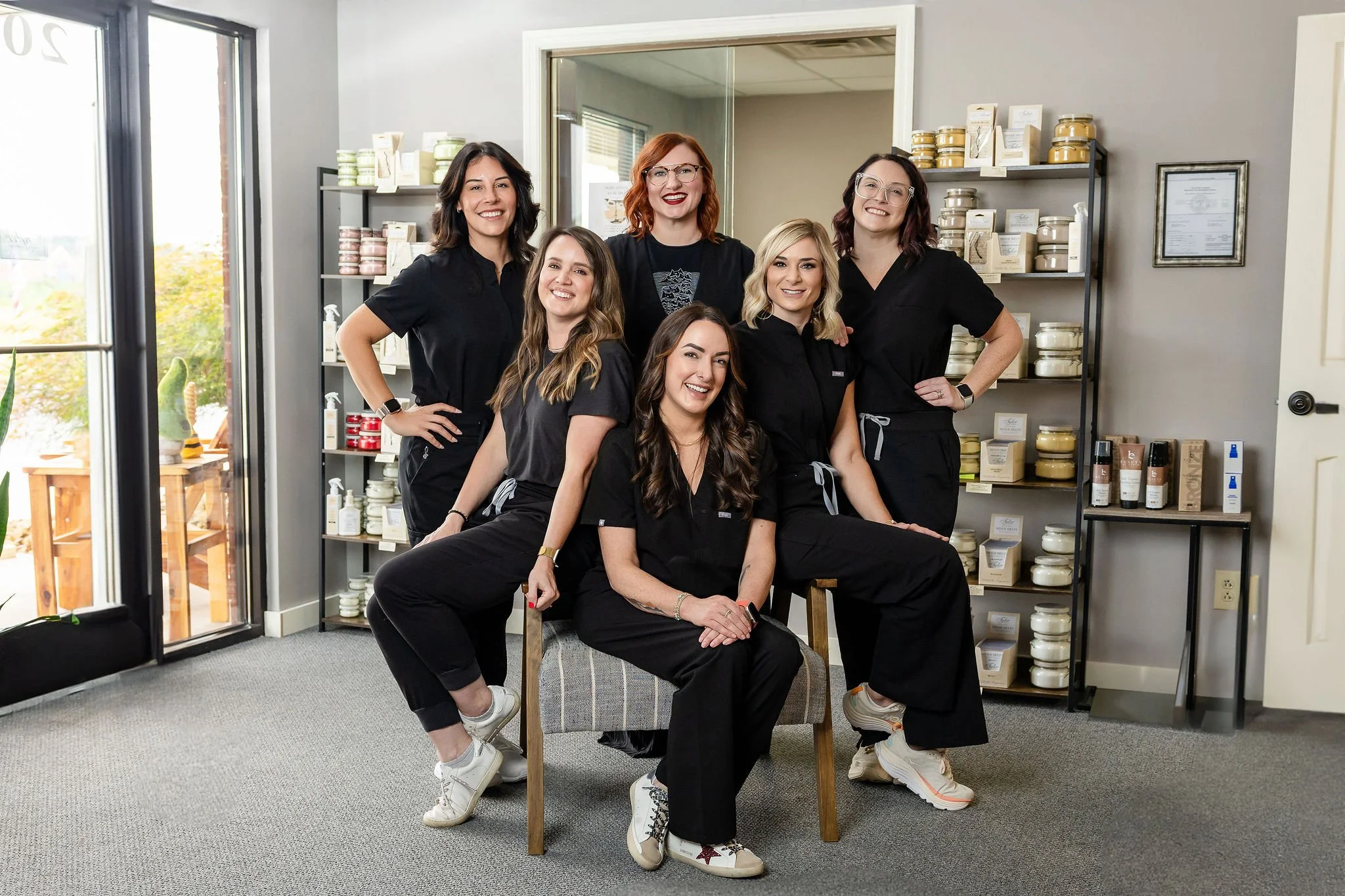 Group of six women posing in a skincare or beauty store, smiling and dressed in black uniforms, with shelves of skincare products in the background.