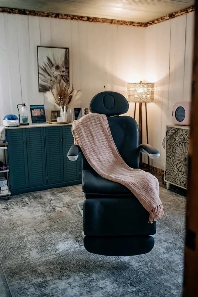 Cozy treatment room at The Collective Med Spa featuring a black aesthetic chair with a soft pink blanket, warm lighting, and a relaxing, spa-like atmosphere.