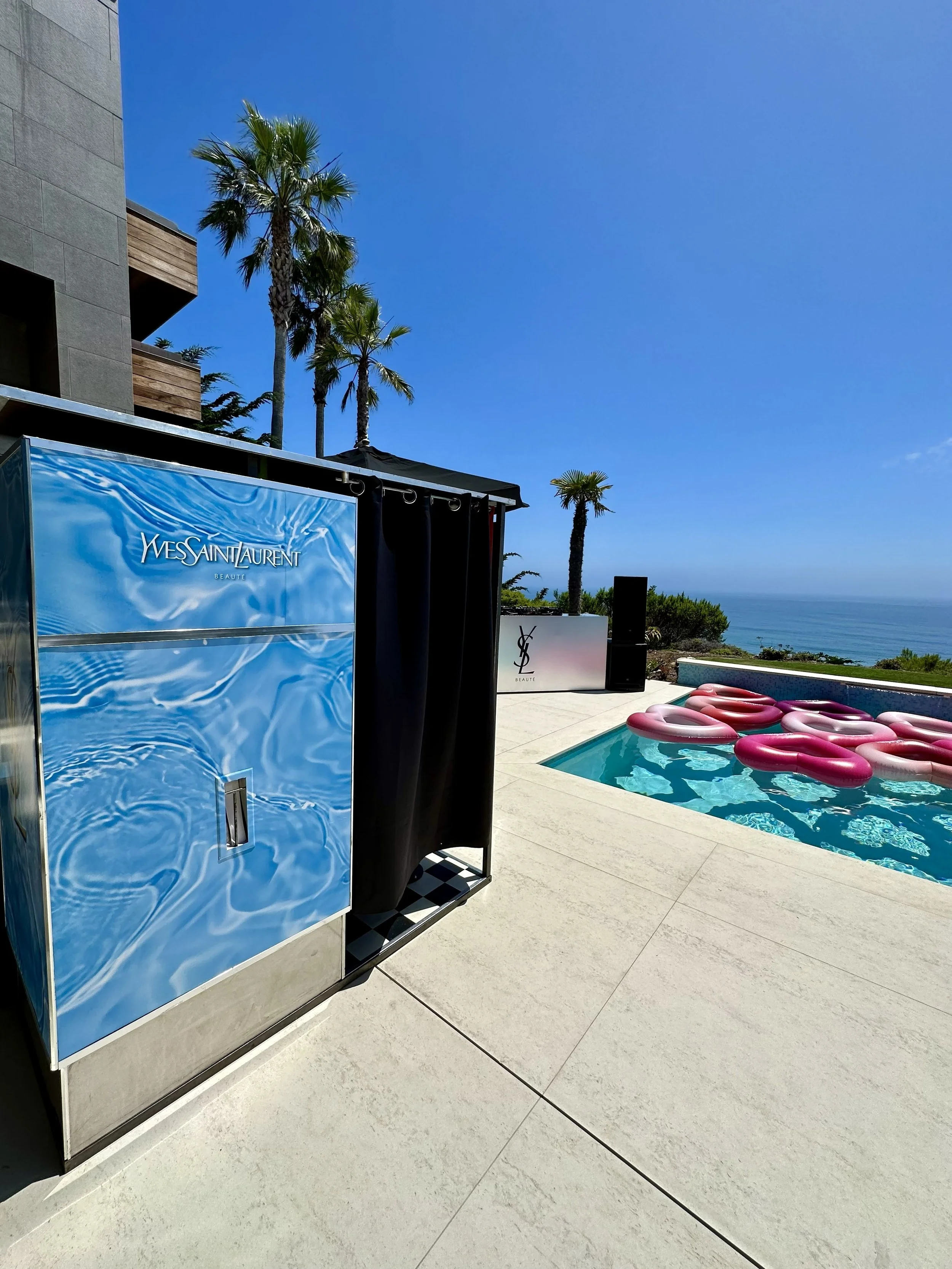 A vintage analog photo booth with a water-like Yves Saint Laurent decal, next to a pool with heart shaped floats.