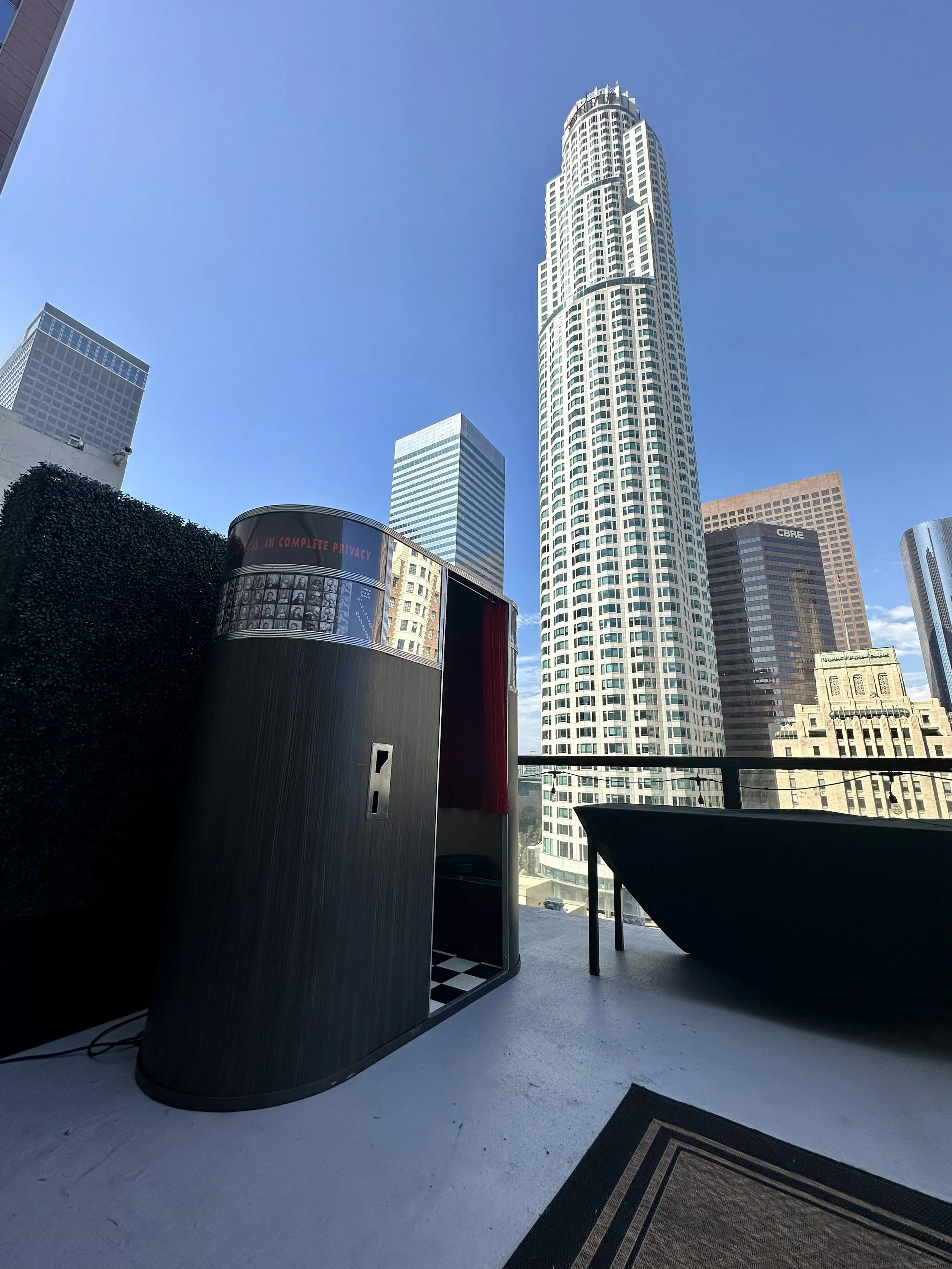 A Model 11 vintage analog photobooth on a high rise rooftop in downtown Los Angeles with the iconic building towering over close in the background.
