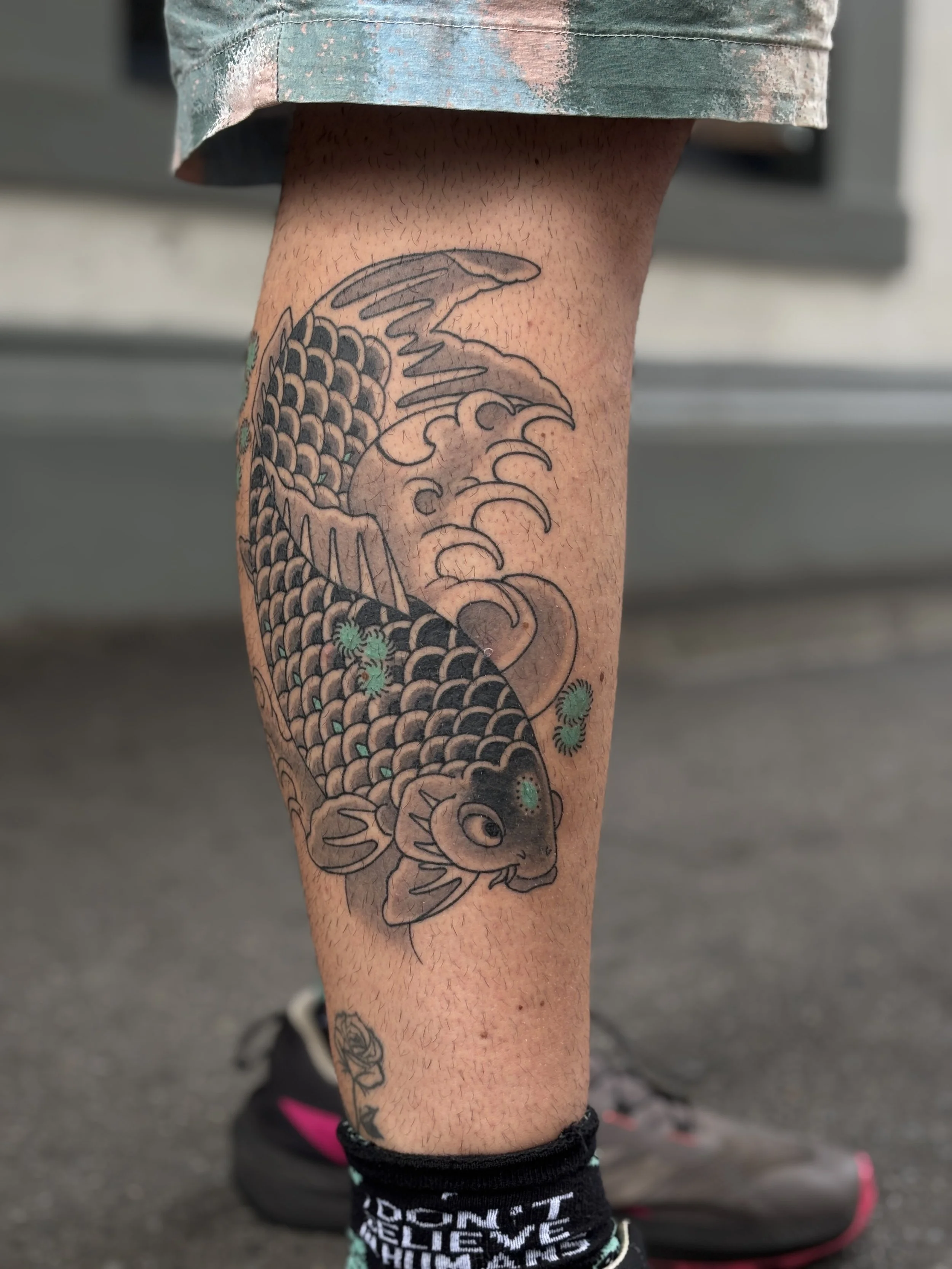 Tattoo of a traditional Japanese koi fish on a person's calf, with detailed scales, flowing fins, and water accents, on light skin.