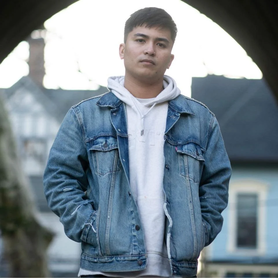 A person wearing a denim jacket over a hoodie, standing outdoors.