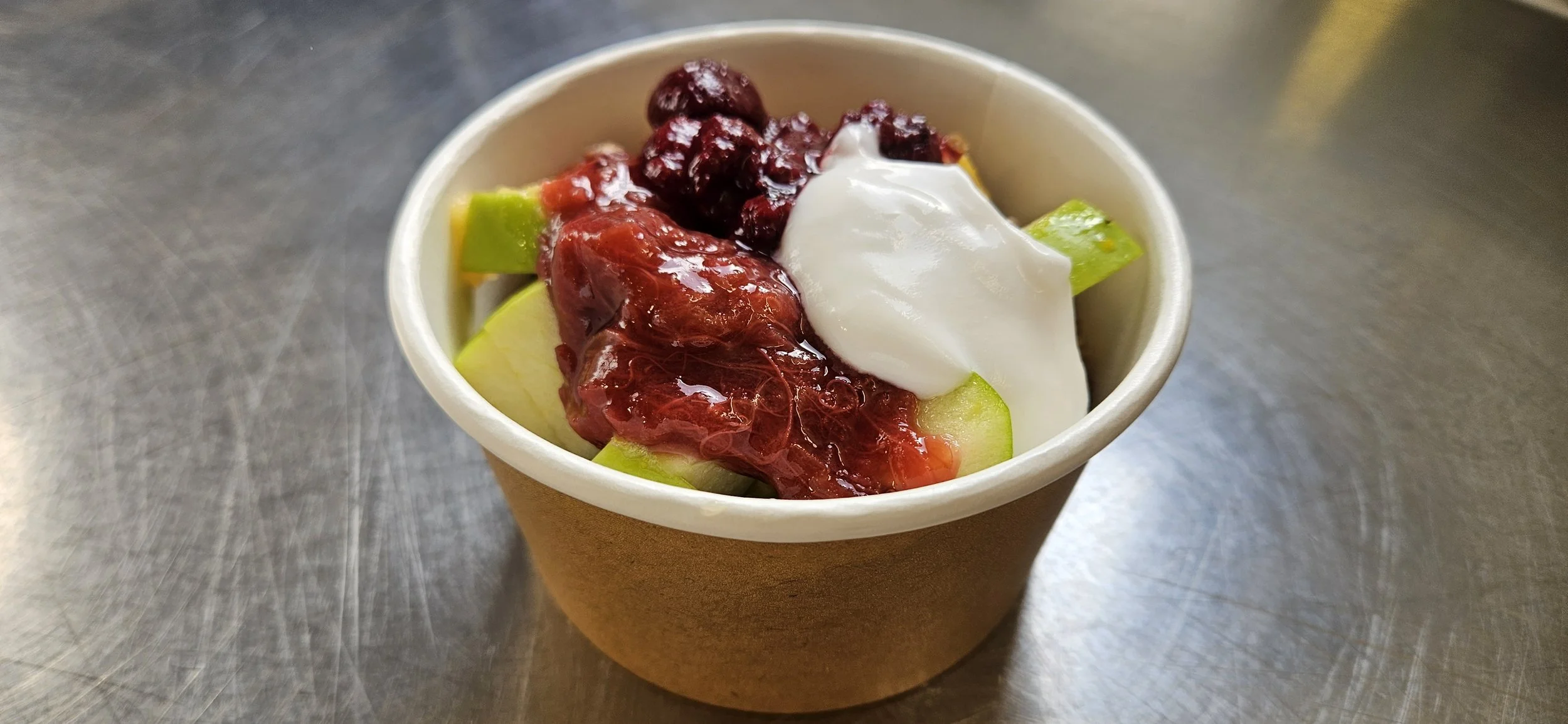 A paper cup filled with chopped green melon, topped with whipped cream, cranberry sauce, and whole cranberries.