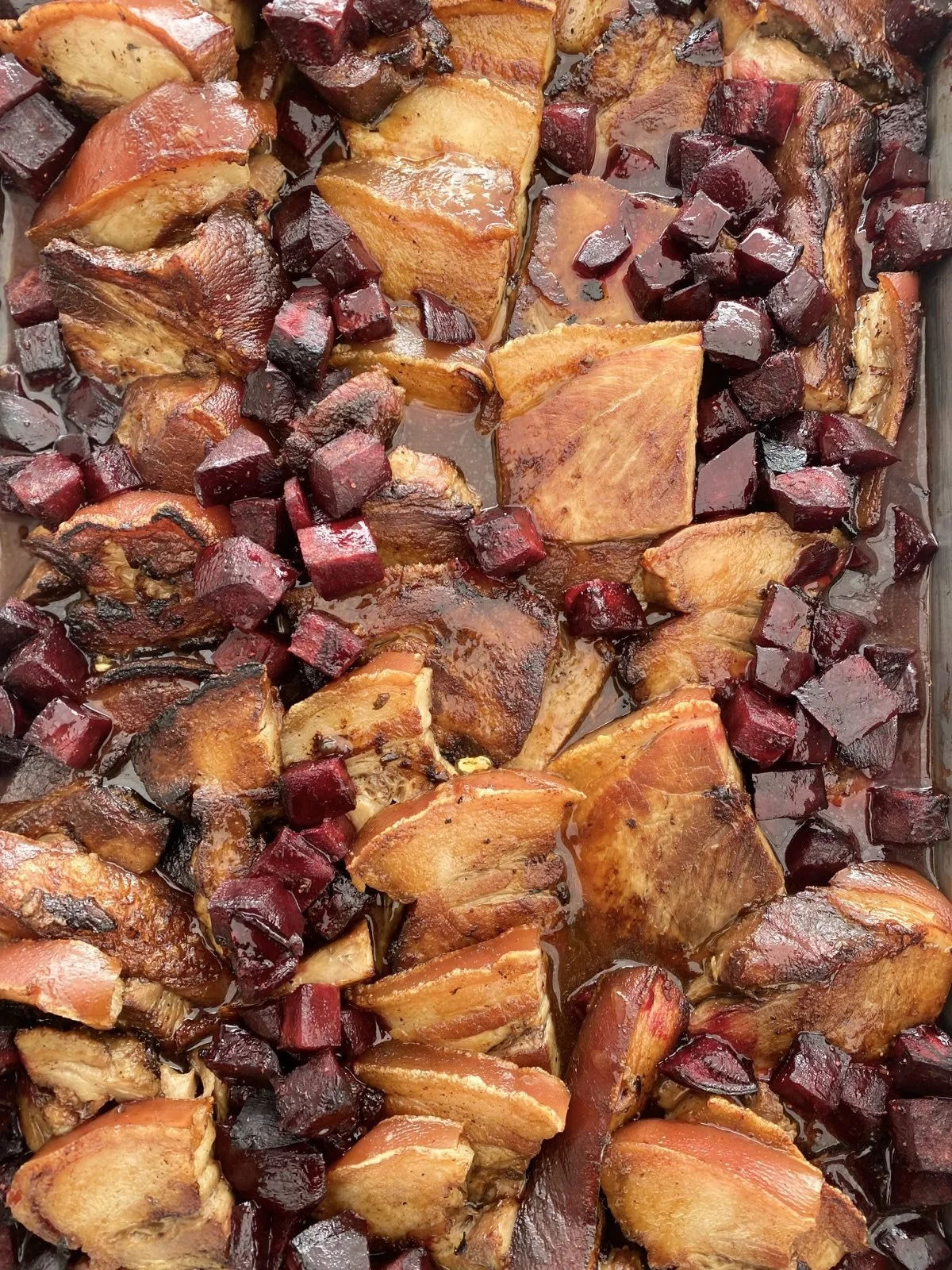 Roasted free range pork shoulder, potatoes and beets in a baking dish.