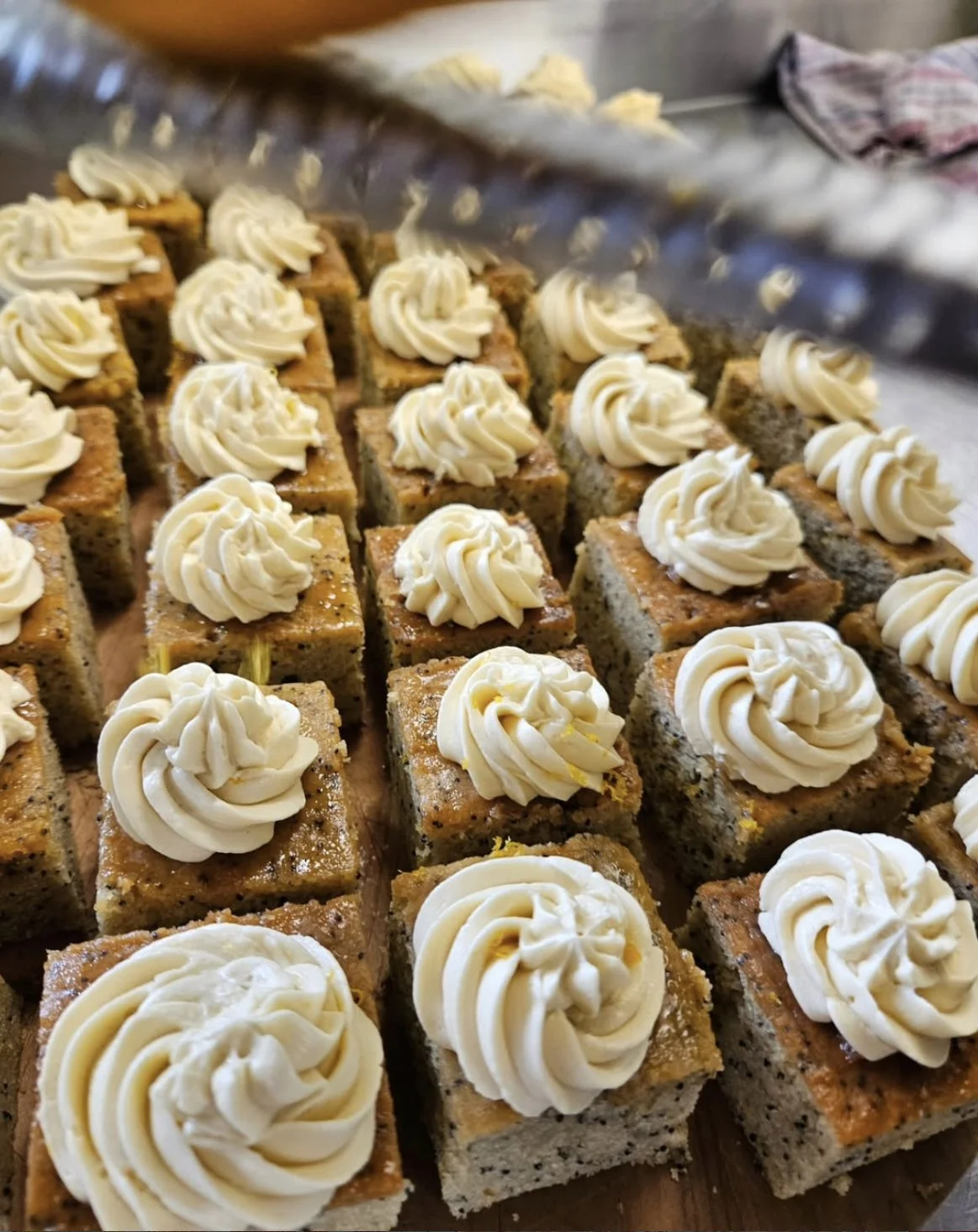 Close-up of square pieces of a banana cake topped with swirls of white frosting, arranged on a tray.