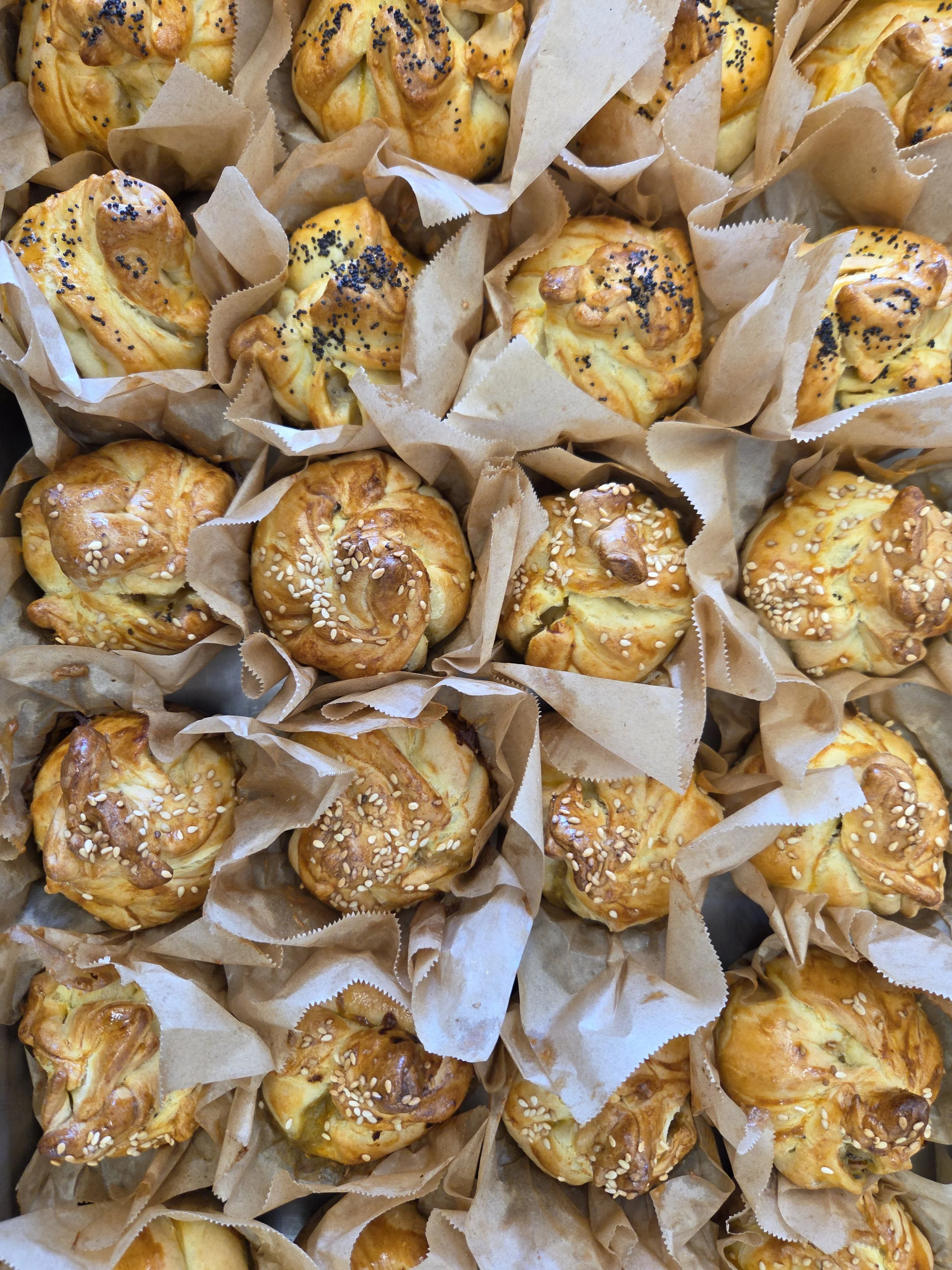 Close-up of homemade baked pastries, some with sesame seeds and others with poppy seeds, resting in paper muffin cups.