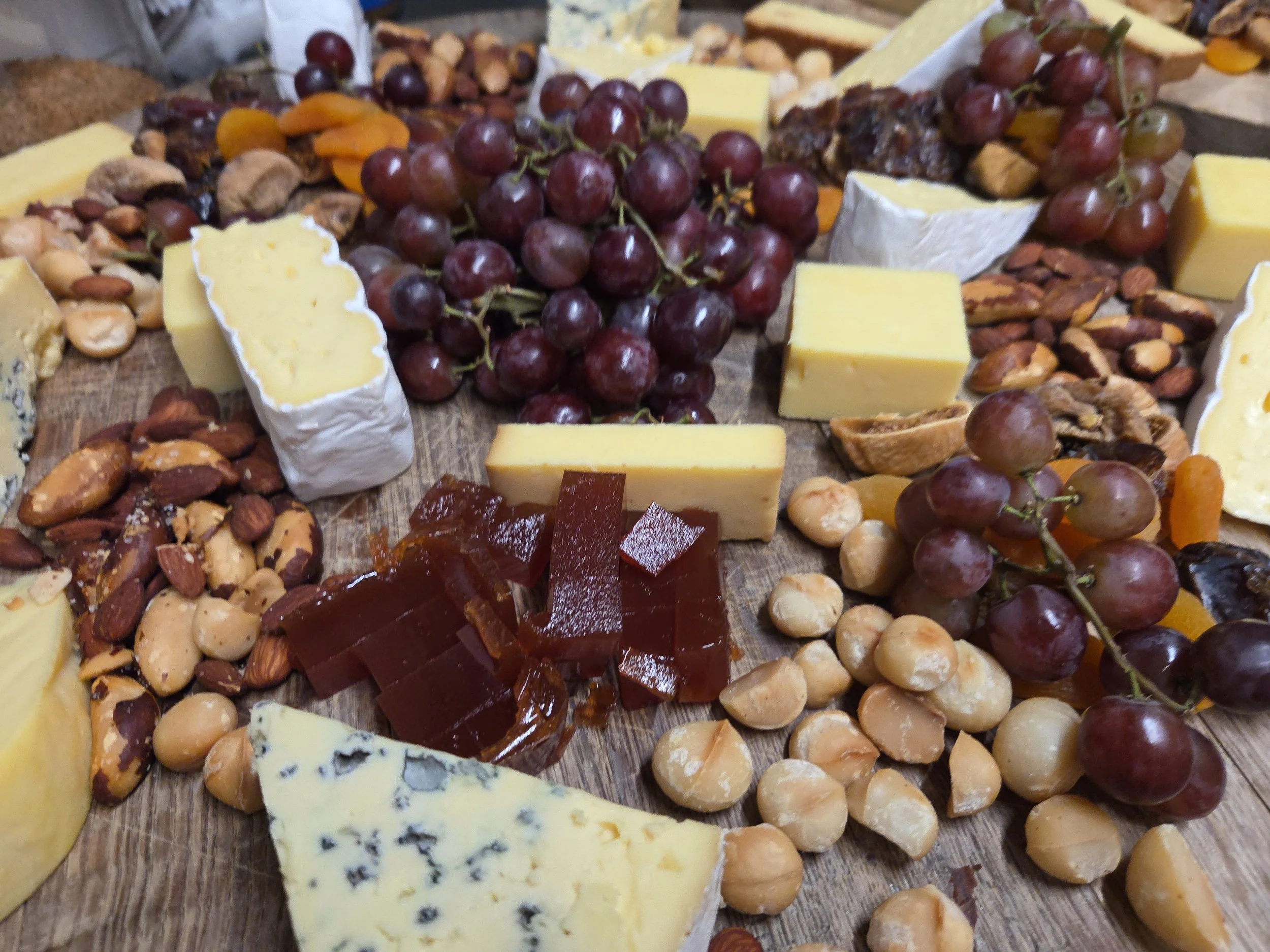 A cheese platter with various types of cheese, grapes, nuts, dried fruit, and crackers arranged on a wooden board.