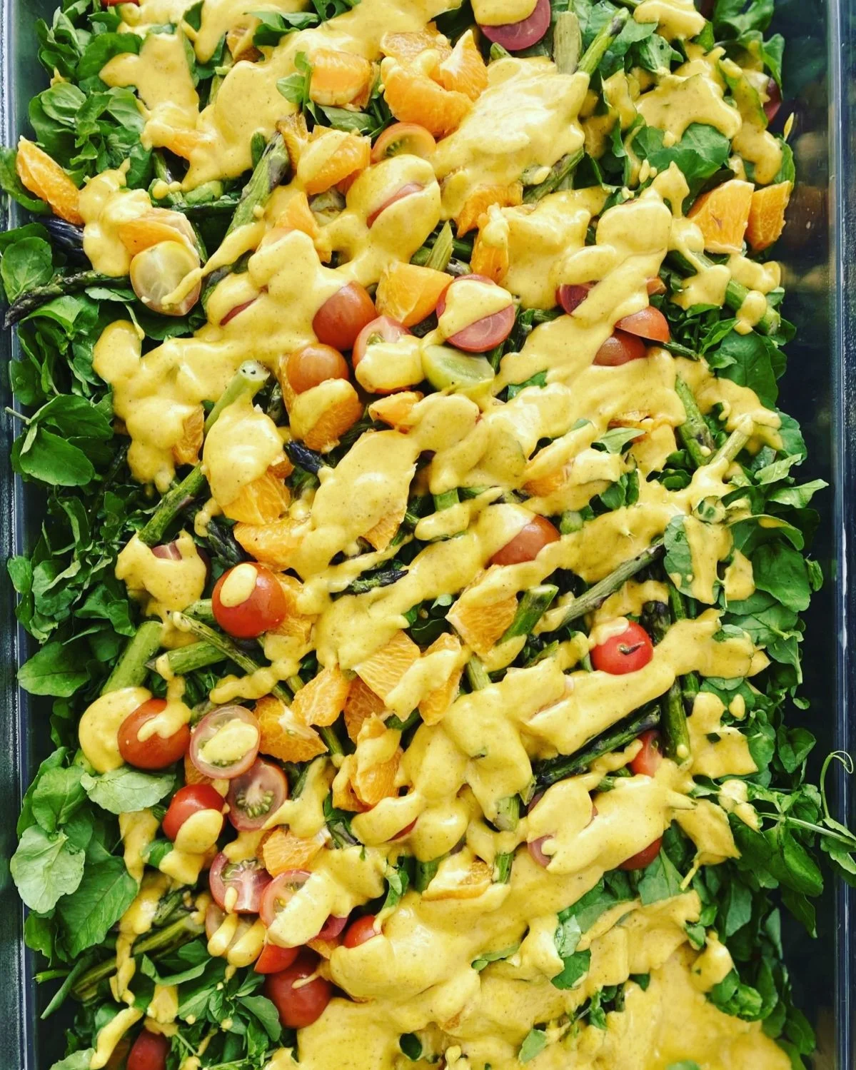 Mixed salad with cherry tomatoes, green leafy vegetables, and yellow salad dressing drizzled on top.