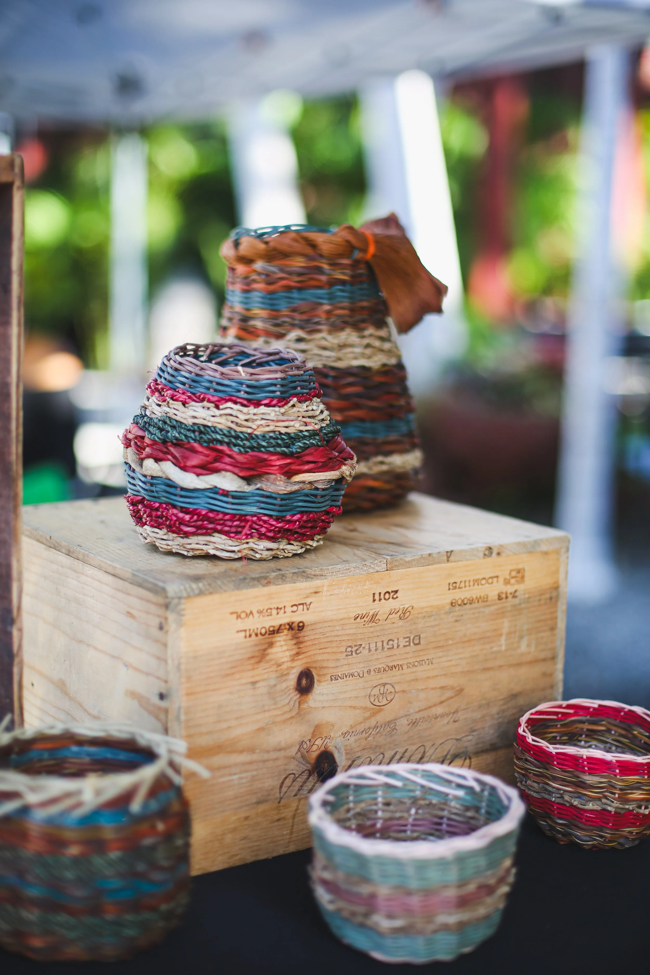 Various woven baskets and vases made from natural fibers displayed on tables at an outdoor market or craft fair.