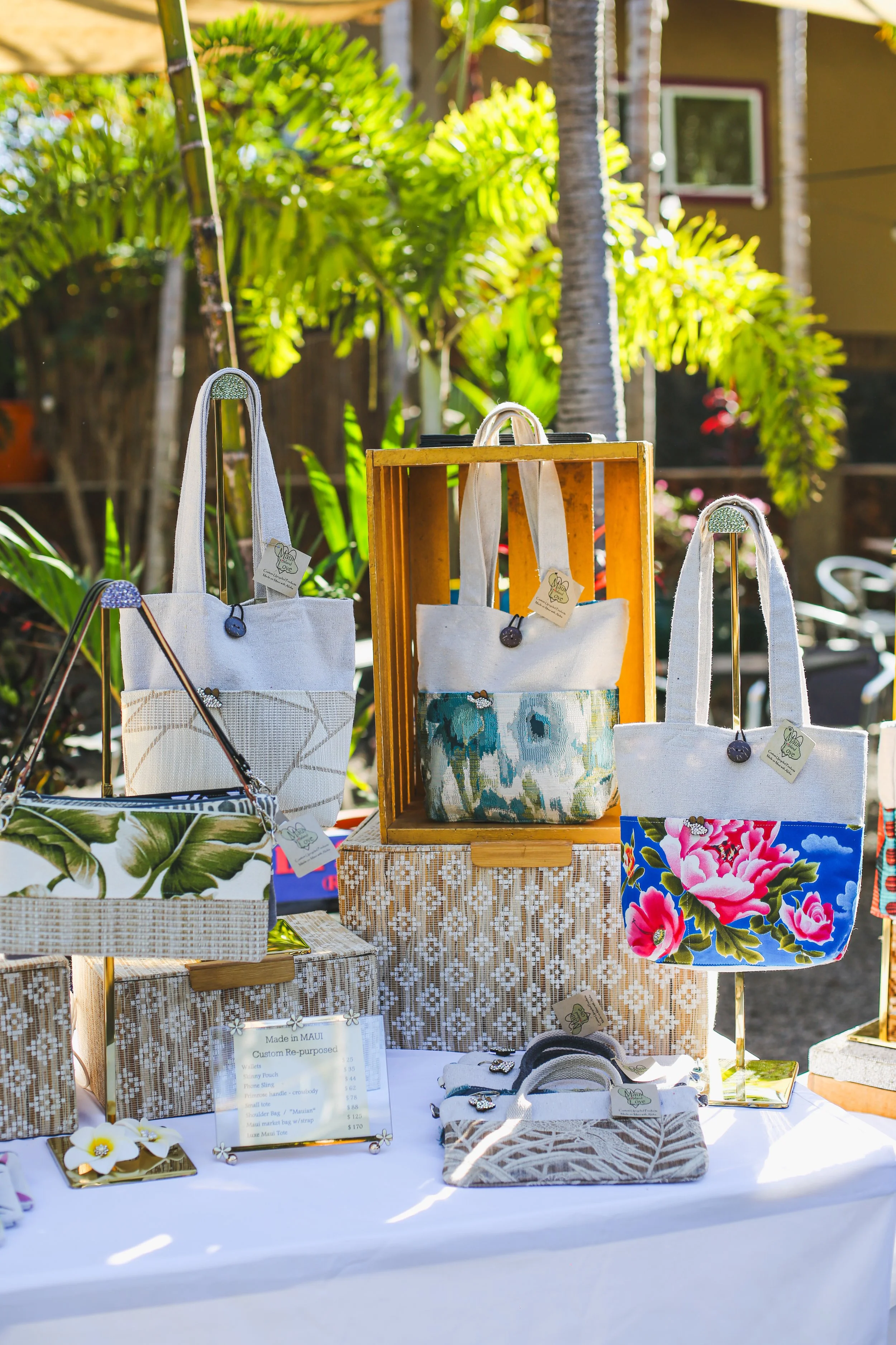 Display of upcycled fabric tote bags with floral patterns at a craft market.