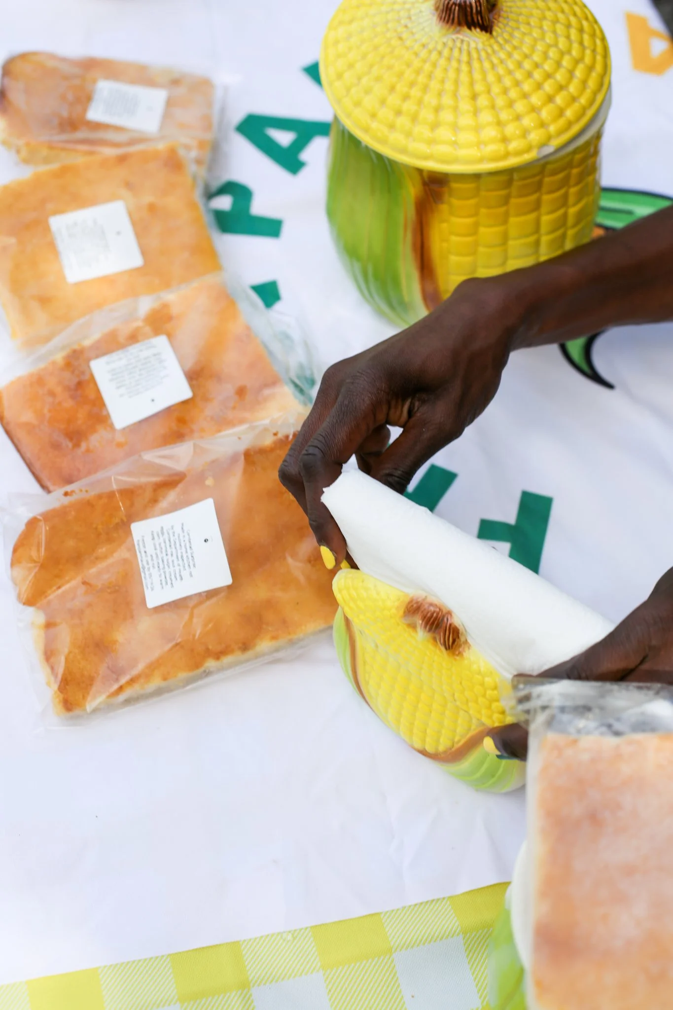 A table with homemade bread and kitchenware, covered with a cloth that has a logo of a cast iron skillet and the text 'Fran Pan Community, Corner Bread for the Community'.
