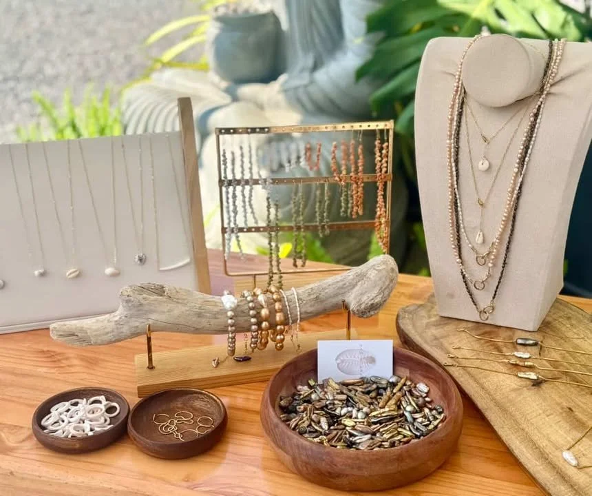 Jewelry display table with necklaces, bracelets, earrings, and rings on wooden and fabric stands, with shells and decorative elements.