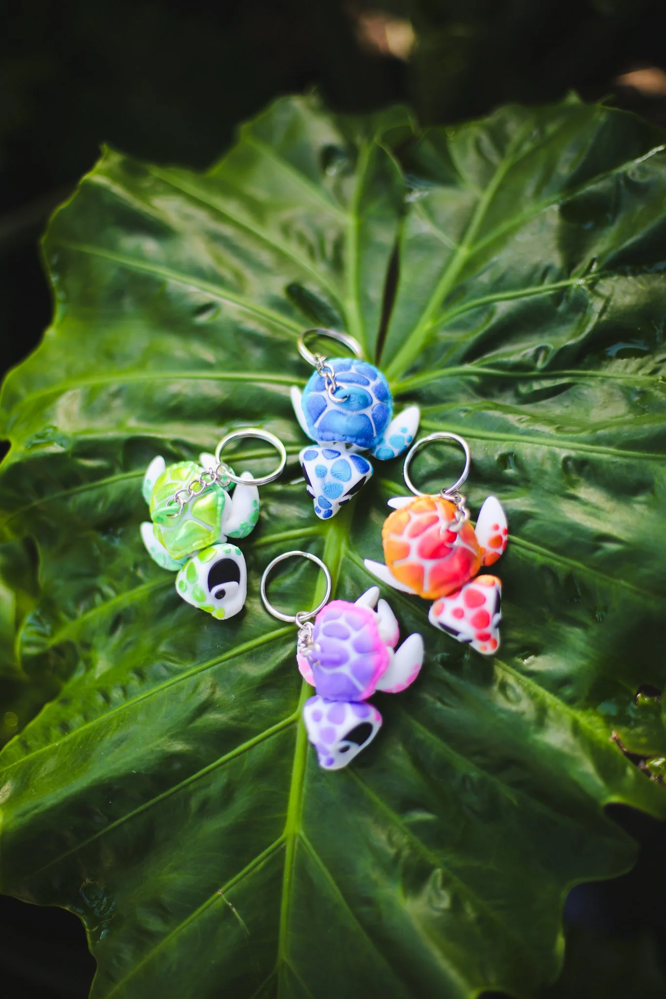 Colorful turtle-shaped keychains with various colors, placed on a large green leaf.