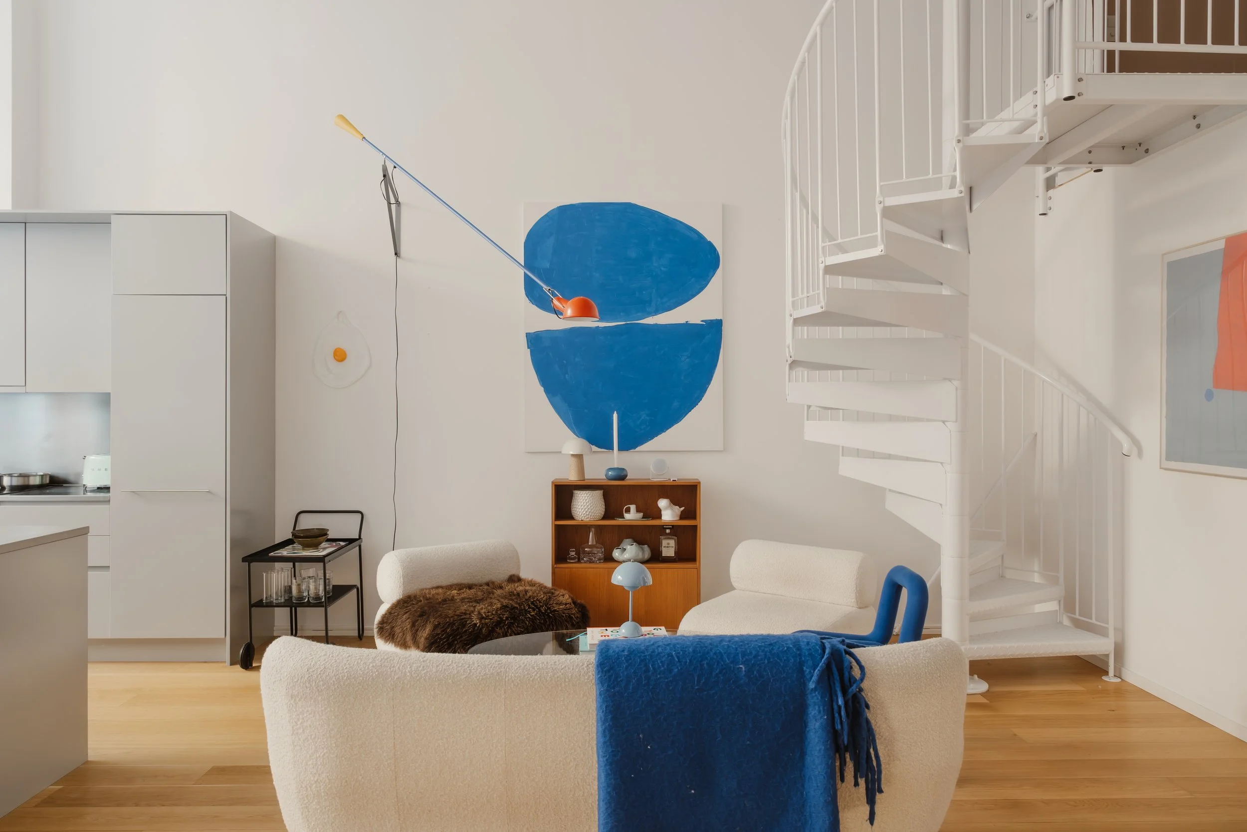 Vardagsrum med beige soffor, ett bokskåp, en spiraltrappa, väggmålning i blått, trämöbler och trägolv.