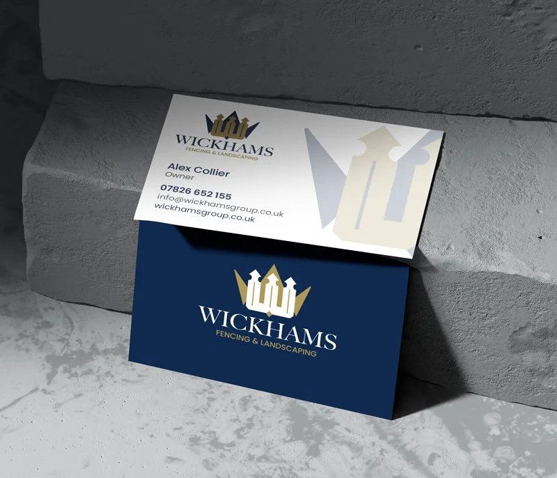 Business cards for Wickhams Fencing & Landscaping, one card with contact info and the other with the company logo, resting on a stone surface.
