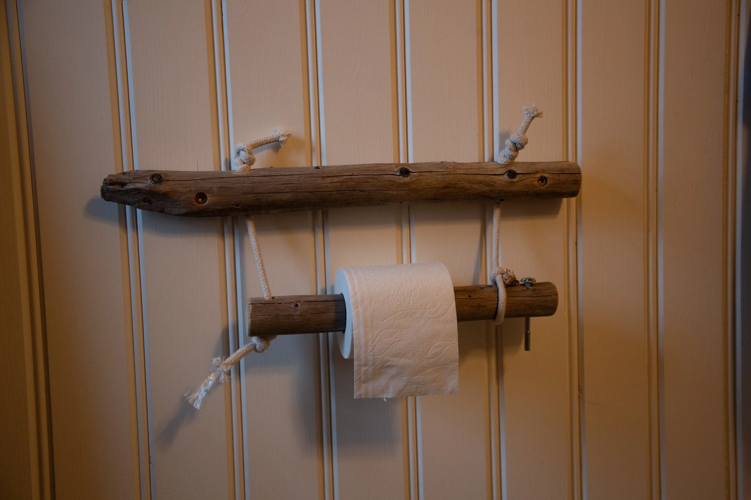 Holzregal mit Seilaufhängung an einer Holzverkleidung, hält eine Papierrolle