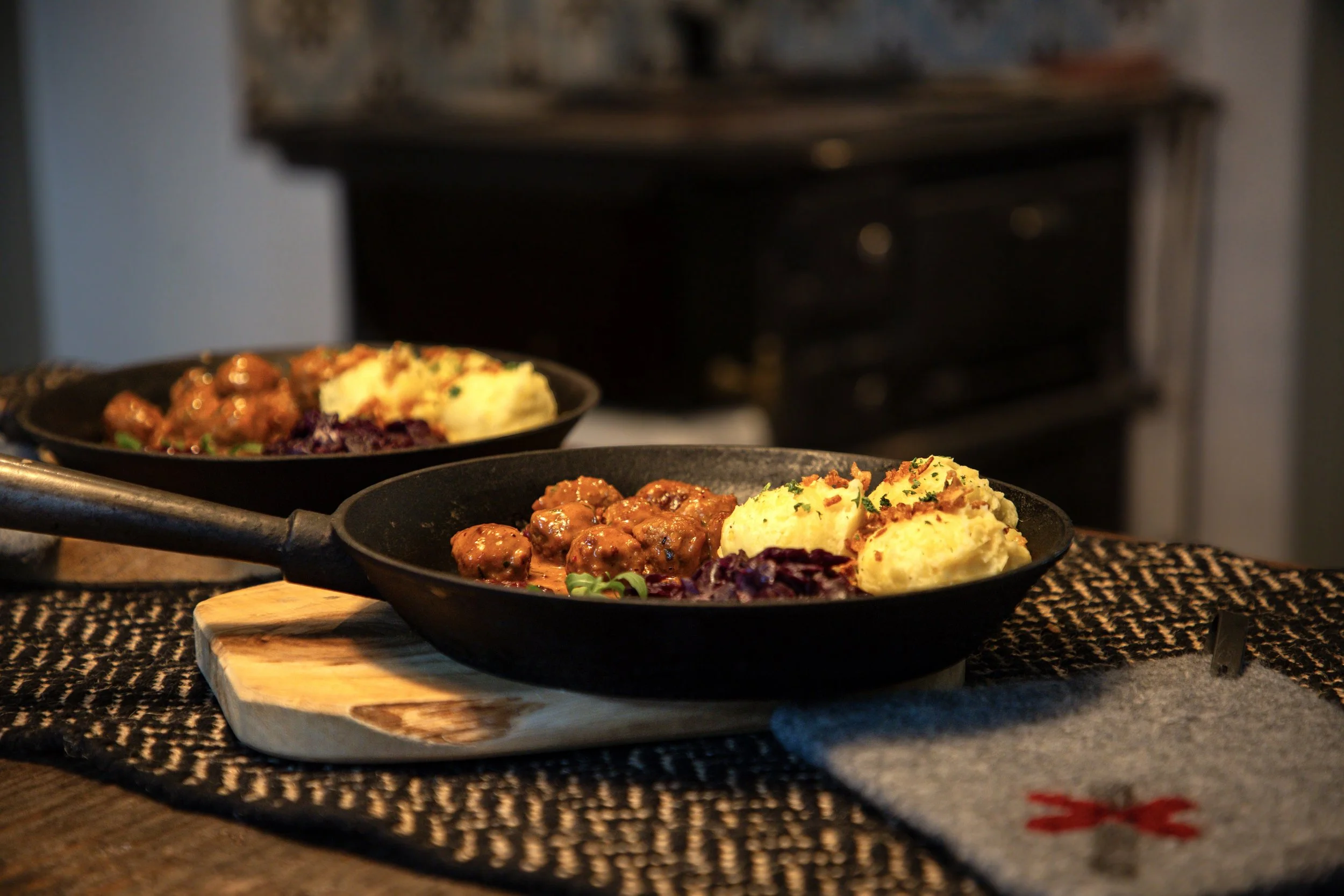 Zwei Pfannen mit Fleischbällchen, Kartoffelpüree und Rotkohl auf einem Holzbrett auf einem Tisch