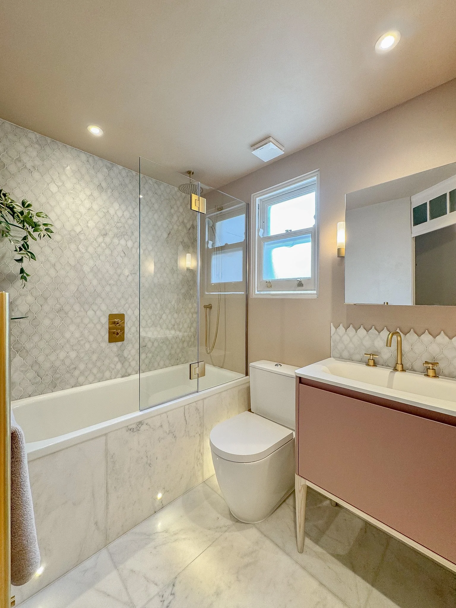 Luxury marble bathroom with brass fittings, bespoke vanity unit and glass bath screen in North London