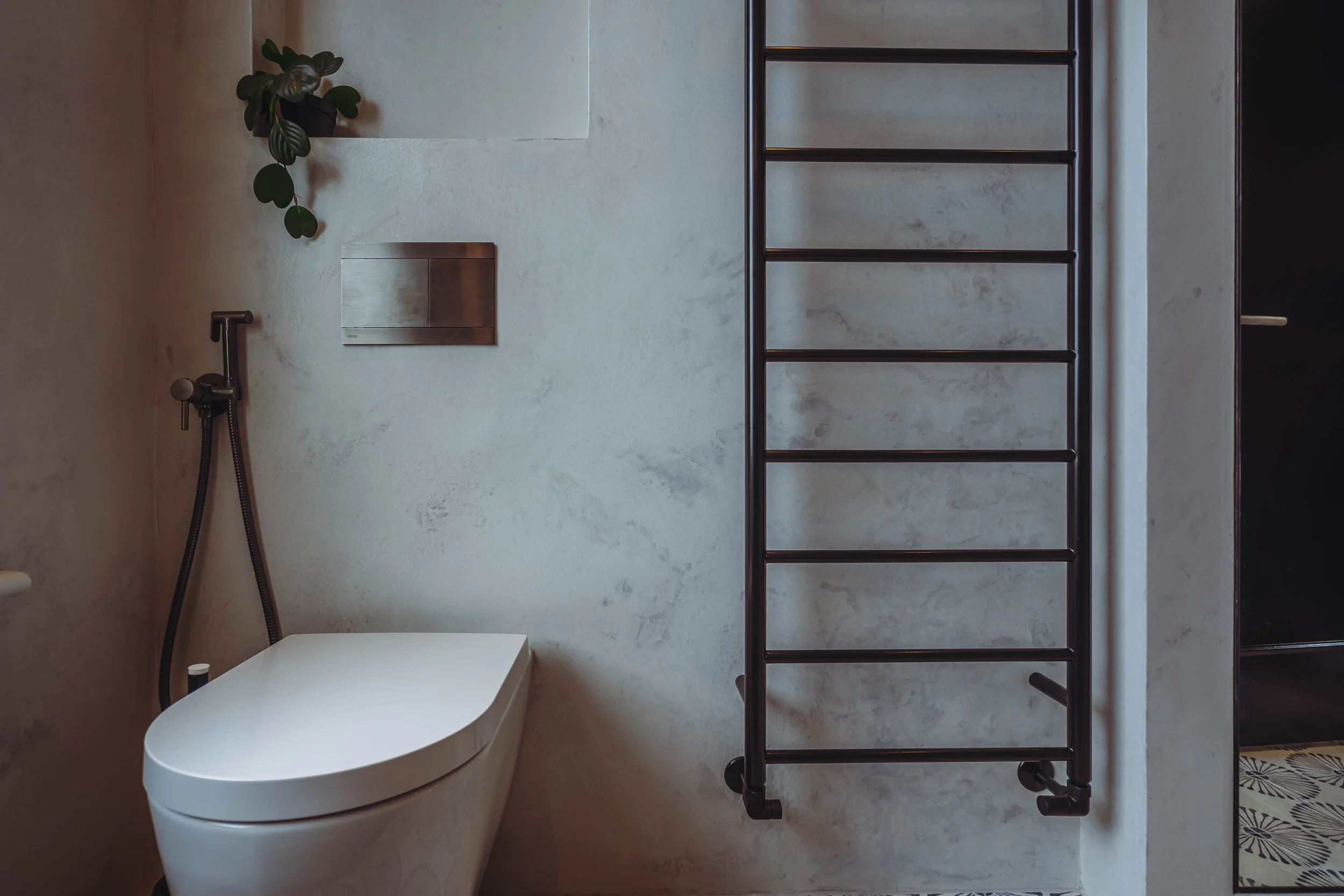 Contemporary bathroom with microcement wall finish, matte black shower handset, concealed flush plate and black heated towel rail