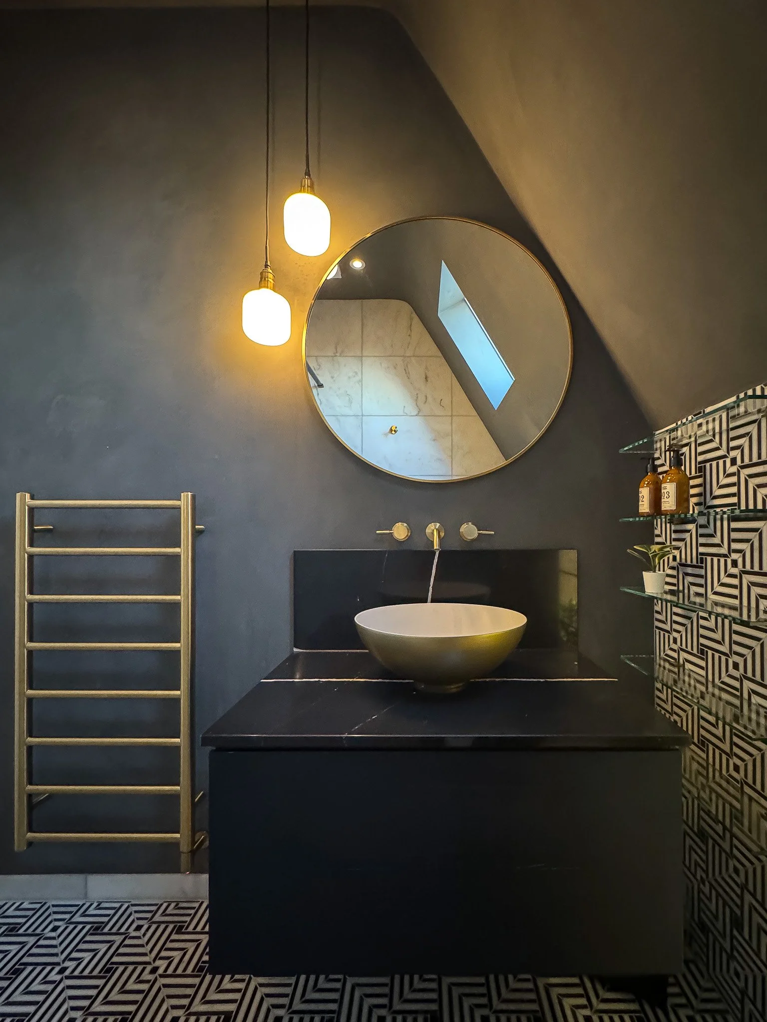 Moody bathroom with black vanity, round mirror and brass fittings in North London