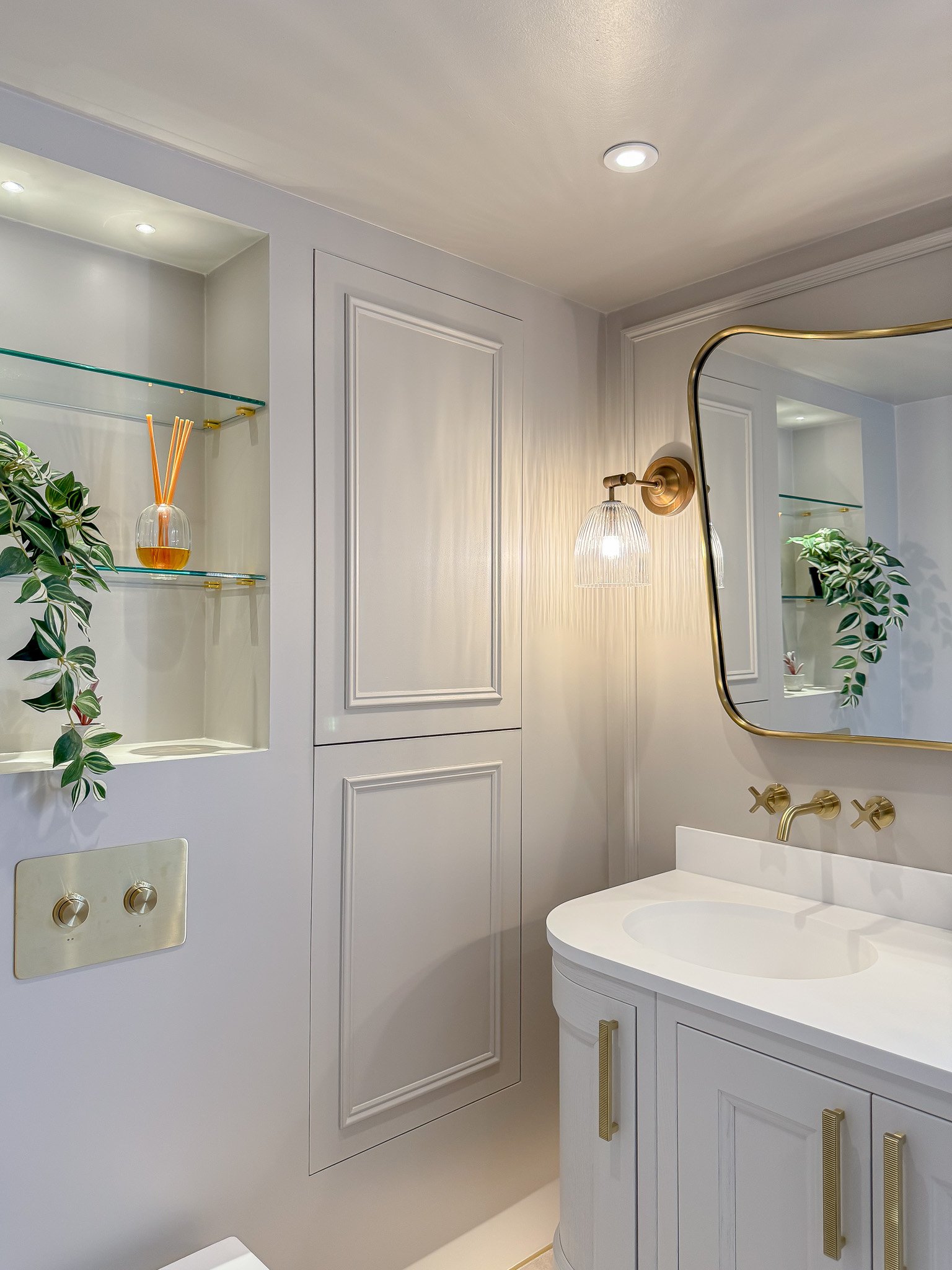 Classic bathroom vanity with bespoke cabinetry, brass wall taps, ribbed glass wall light and recessed shelving in a luxury traditional bathroom