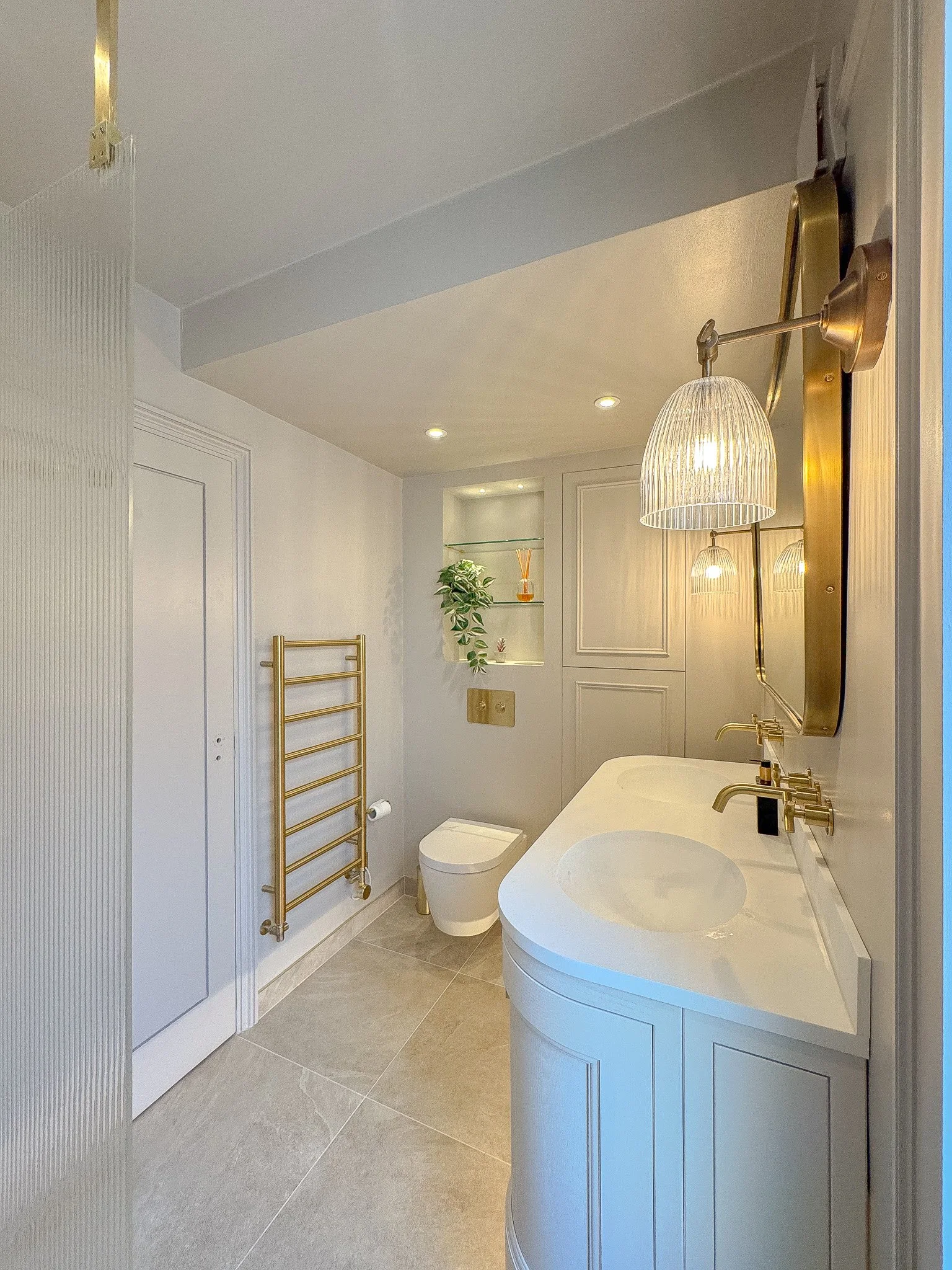 Classic bathroom with curved vanity, brass fittings and wall-mounted towel rail in North London