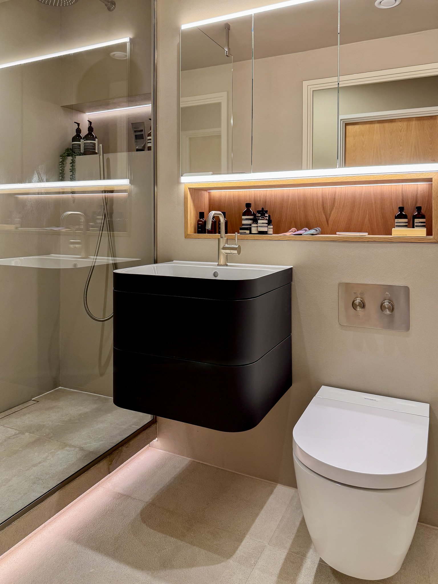 Modern bathroom with wall-hung black vanity unit, recessed shelving and brass tapware in North London