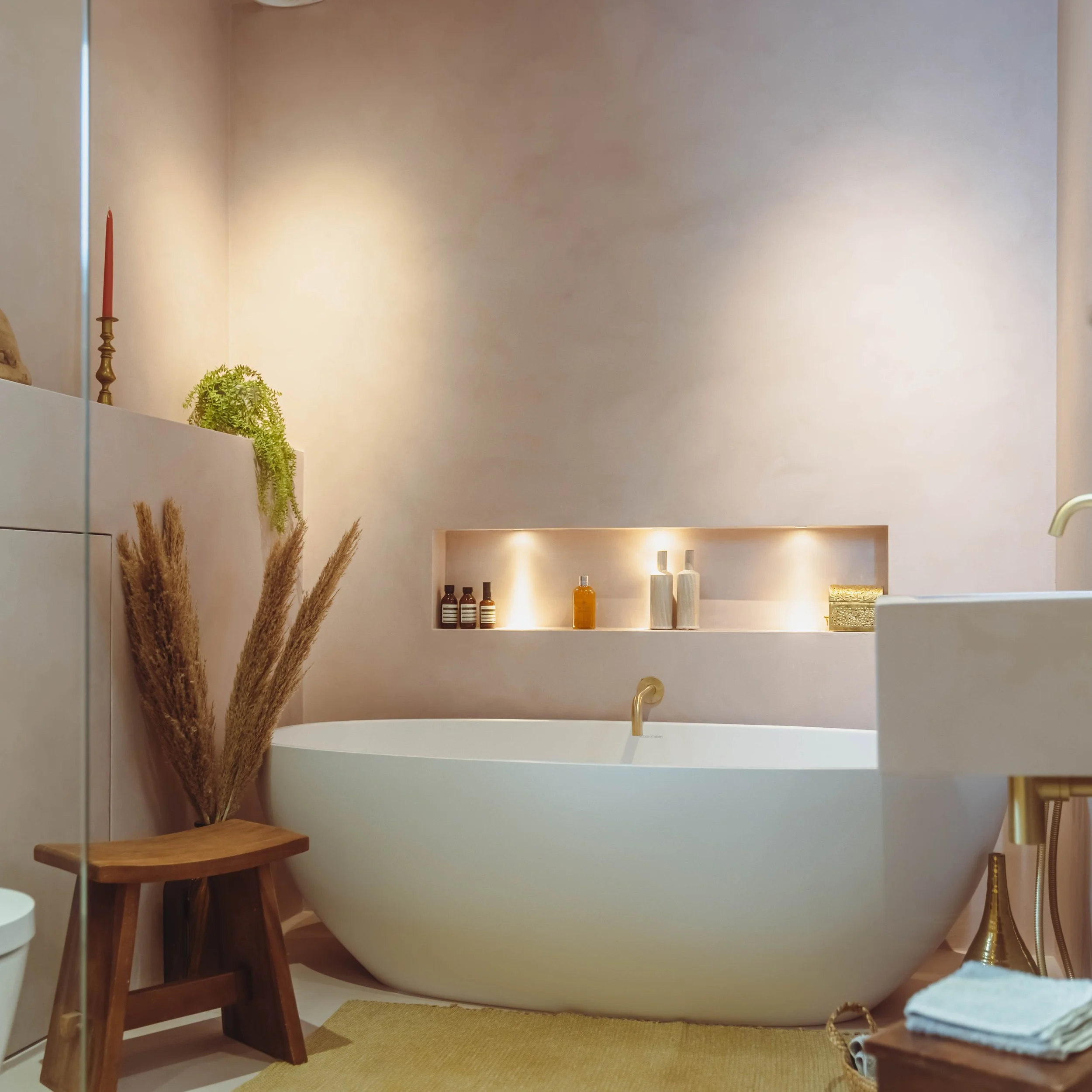 Minimalist bathroom featuring a freestanding bathtub, microcement finish, brass bath filler and softly lit recessed niche