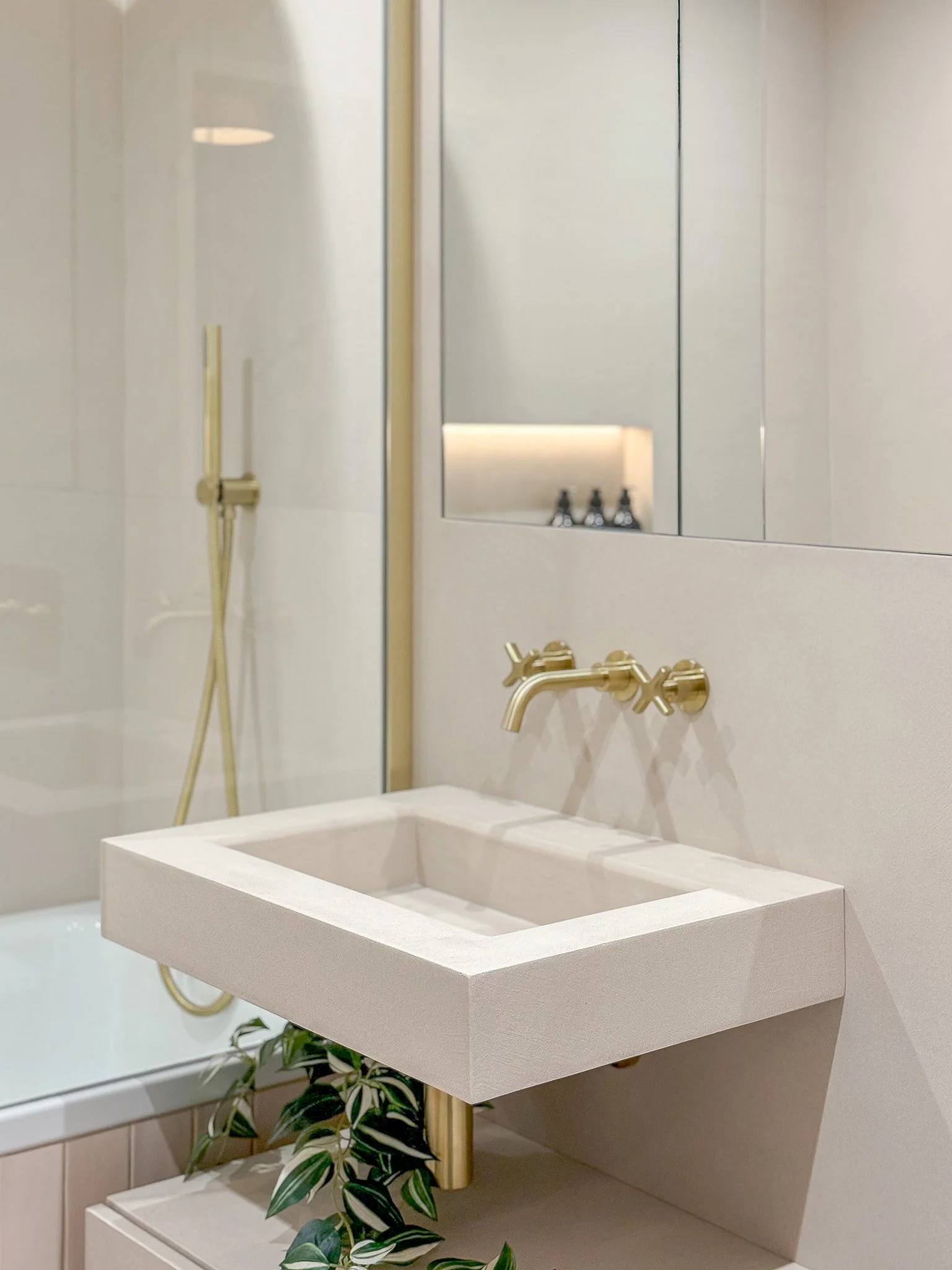 Minimalist wall-mounted basin with stone-effect finish, brushed brass wall taps and mirrored cabinet in a contemporary bathroom