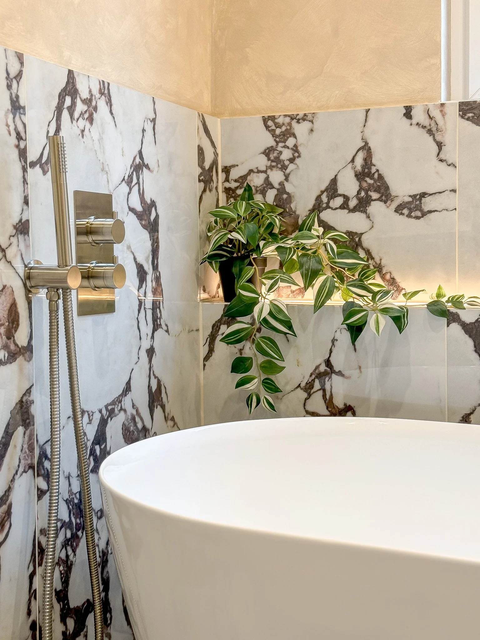 Luxury freestanding bath with marble-effect wall tiles and brushed brass shower fittings by North Arch Bathrooms