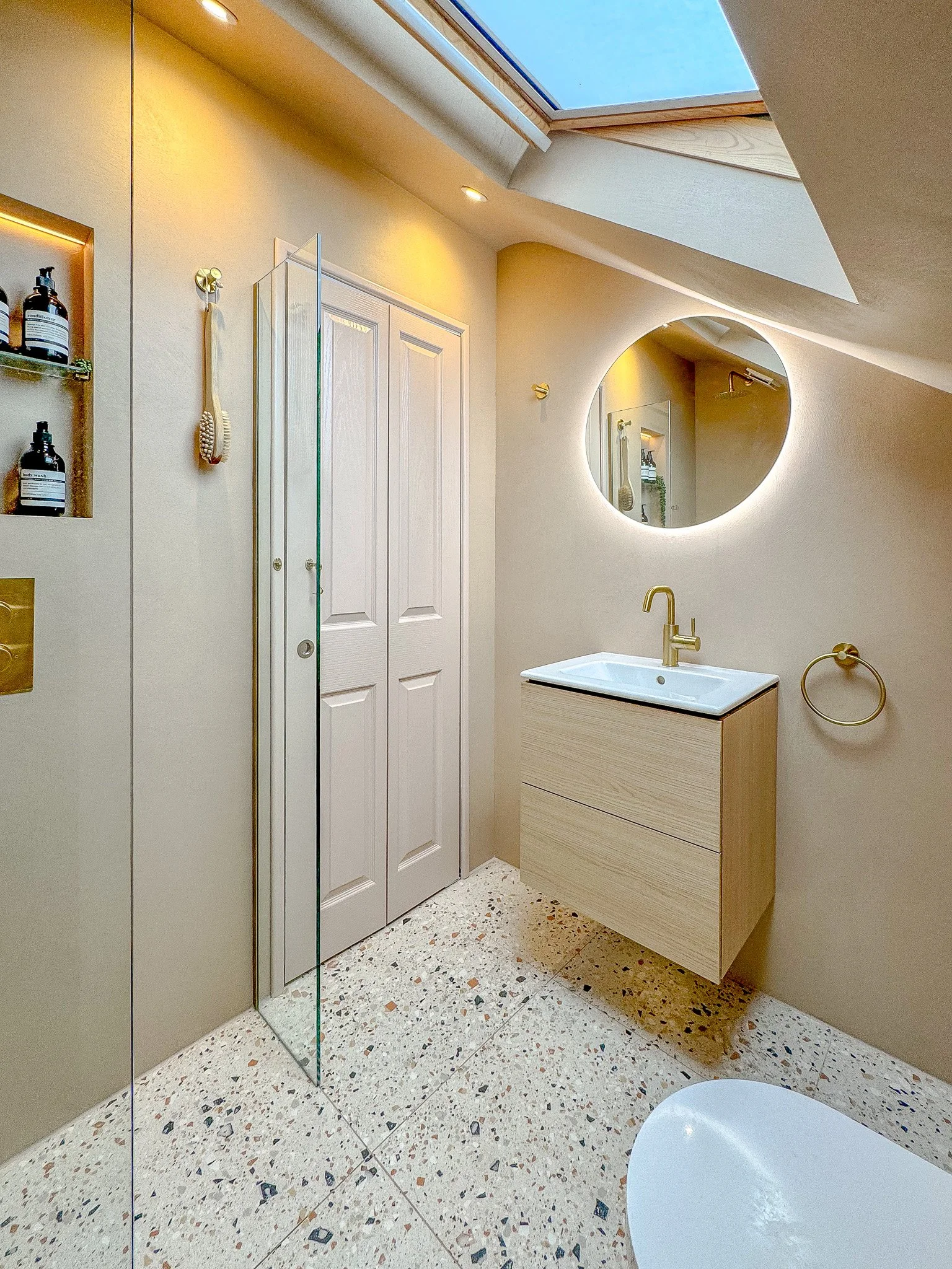 North London bathroom renovation featuring terrazzo tiles, wall-hung vanity, brushed brass fixtures and integrated LED mirror designed by North Arch Bathrooms.